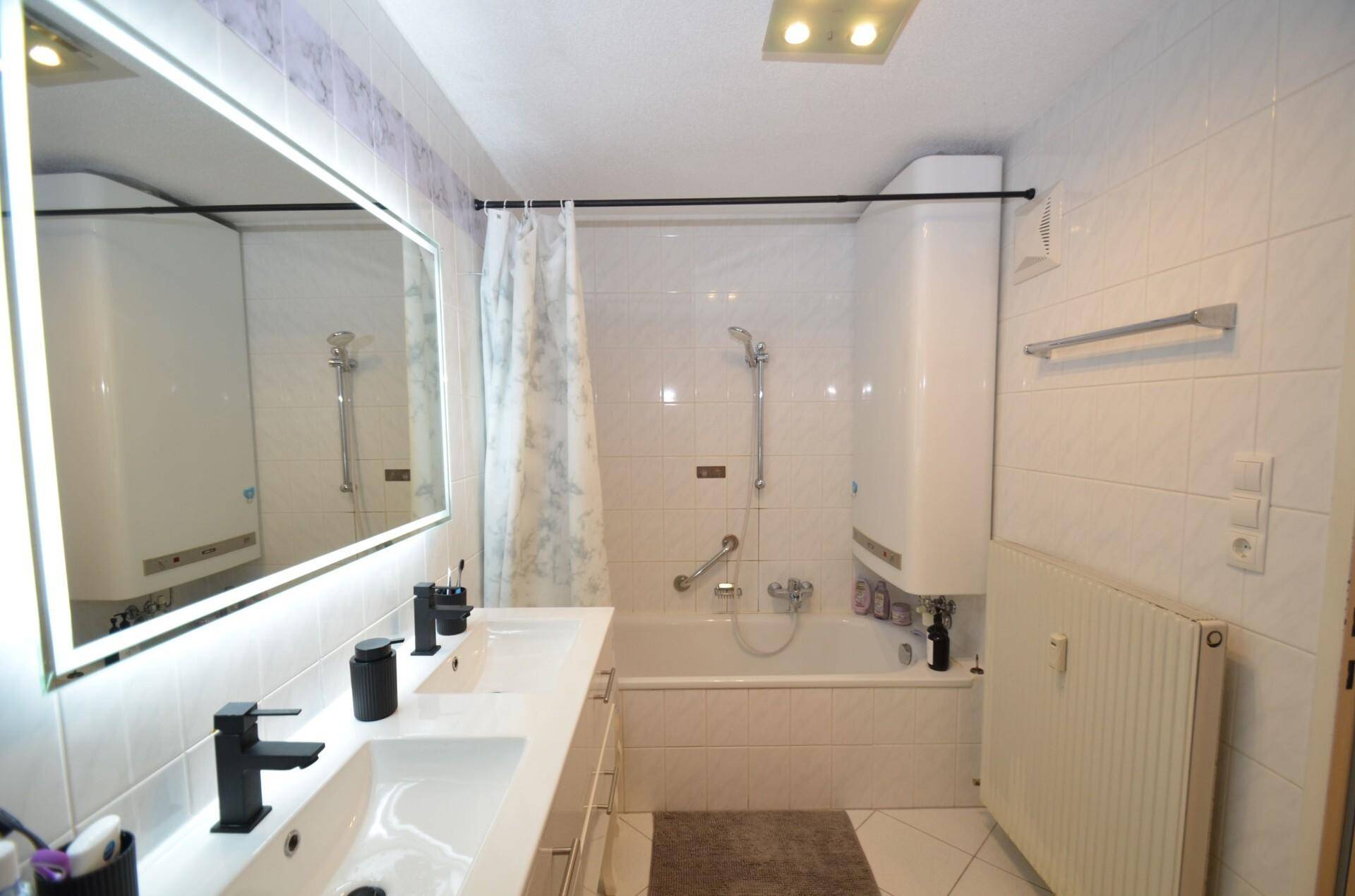 Helles Badezimmer mit weißen Fliesen, Doppelwaschbecken und Badewanne mit Duschvorhang.