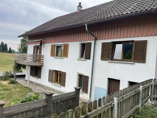 Seitenansicht des Hauses mit Balkon und geöffneten Fensterläden, umgeben von grüner Natur.