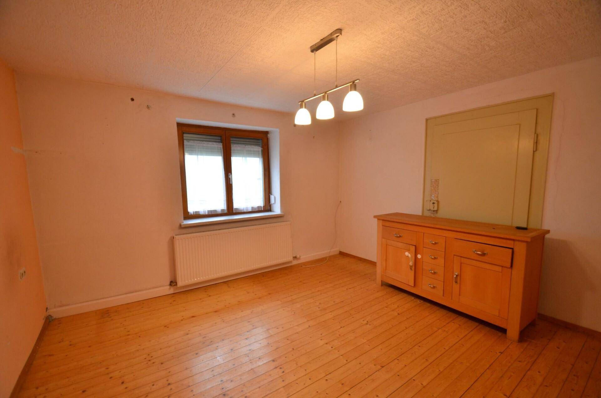Helles Zimmer mit Holzdielenboden, Fenster und einem traditionellen Holzschrank.