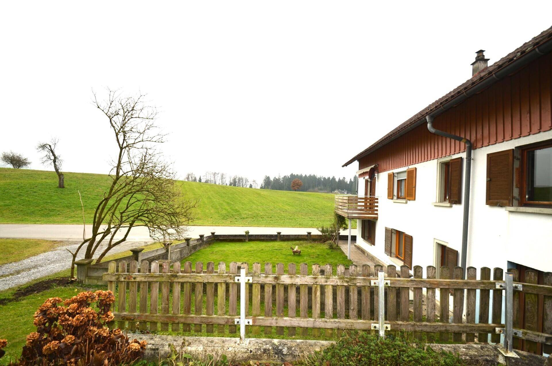 Grüner Gartenbereich neben dem Haus mit Holzzaun und weitem Blick in die Landschaft.