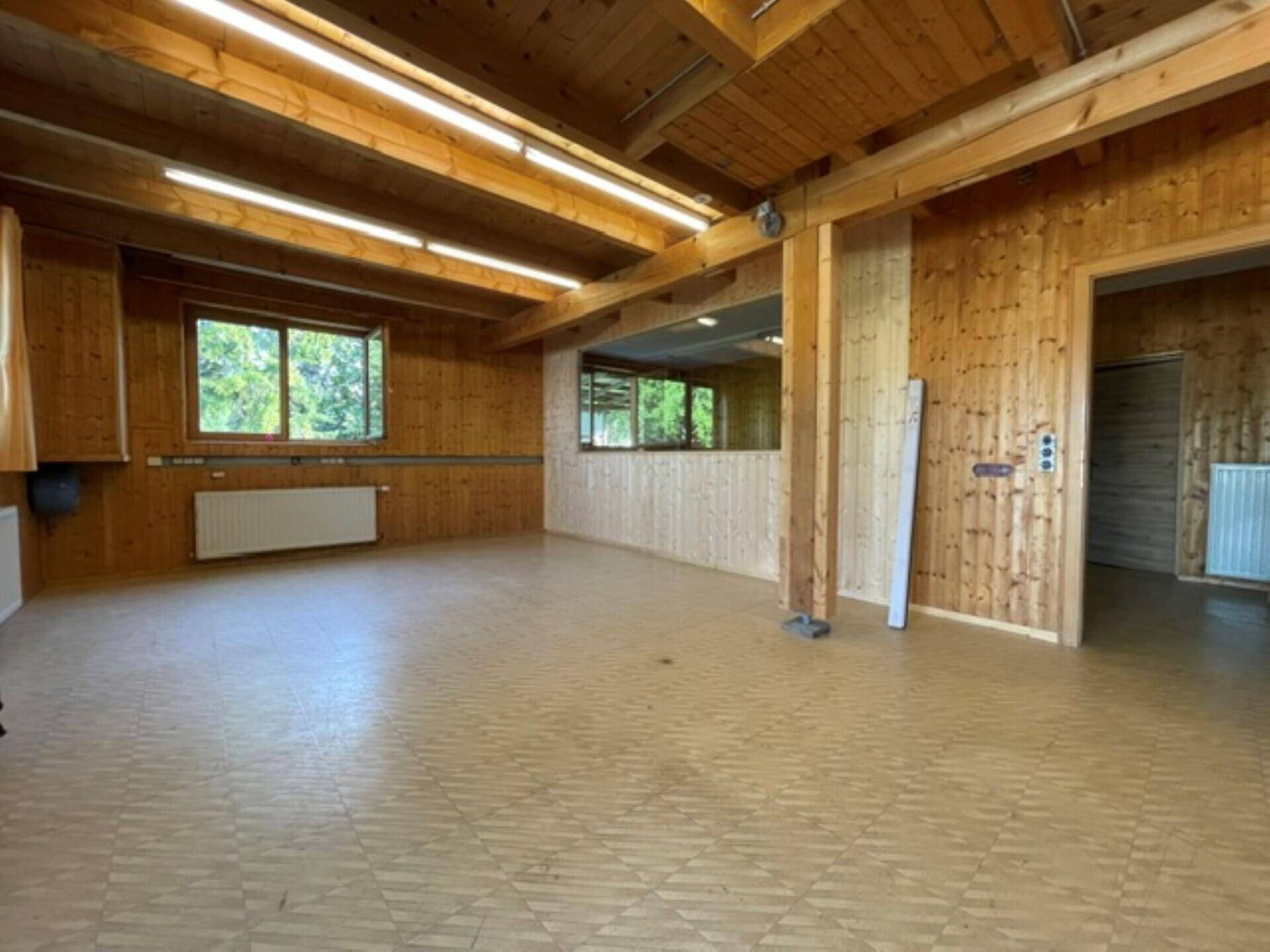 Heller Innenraum mit Holzvertäfelung, Holzbalkendecke und Fenstern, die viel Tageslicht hereinlassen.