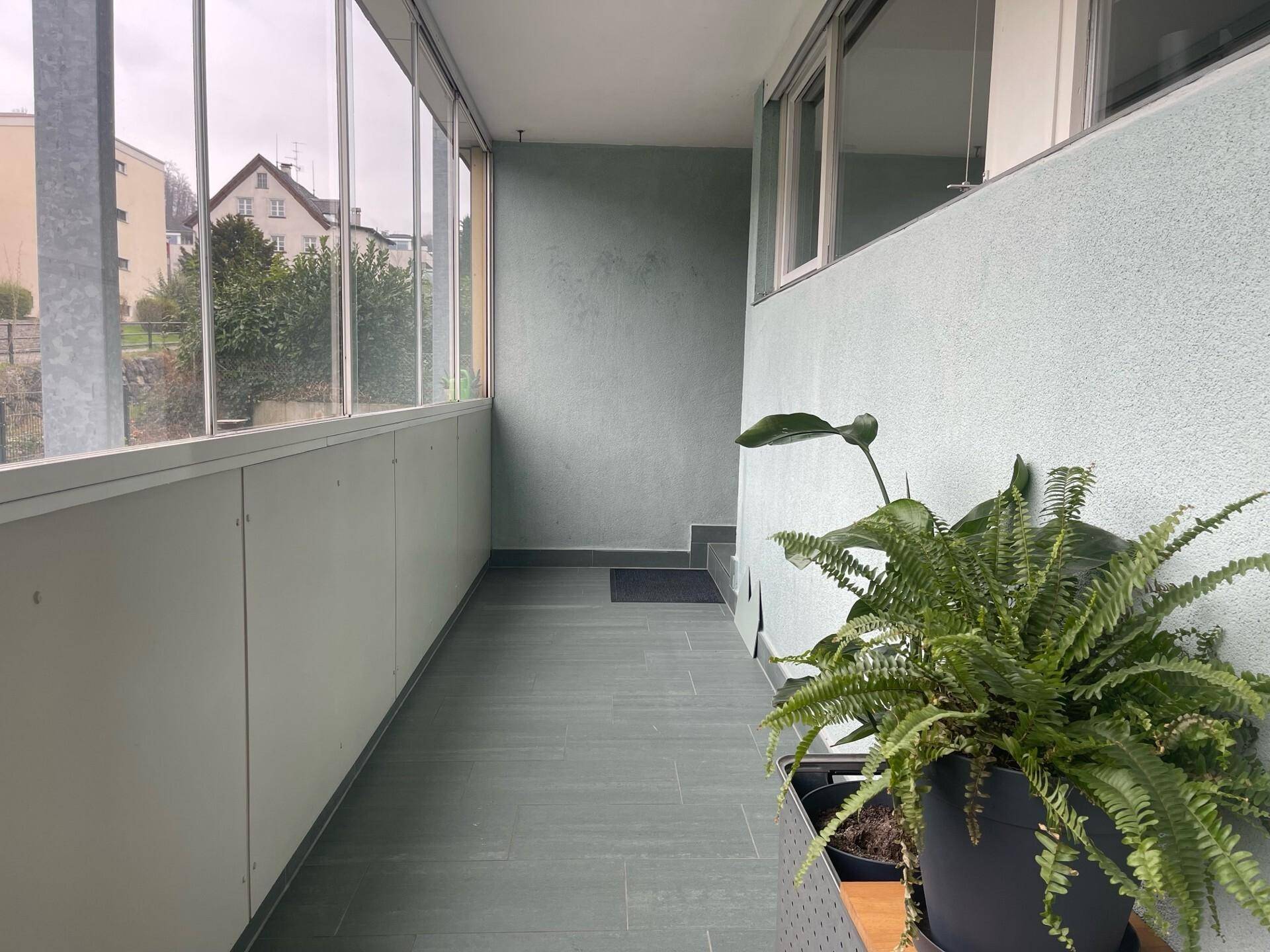 Verglaster Balkon mit Fliesenboden und einer Pflanze, bietet zusätzlichen Wohnraum.