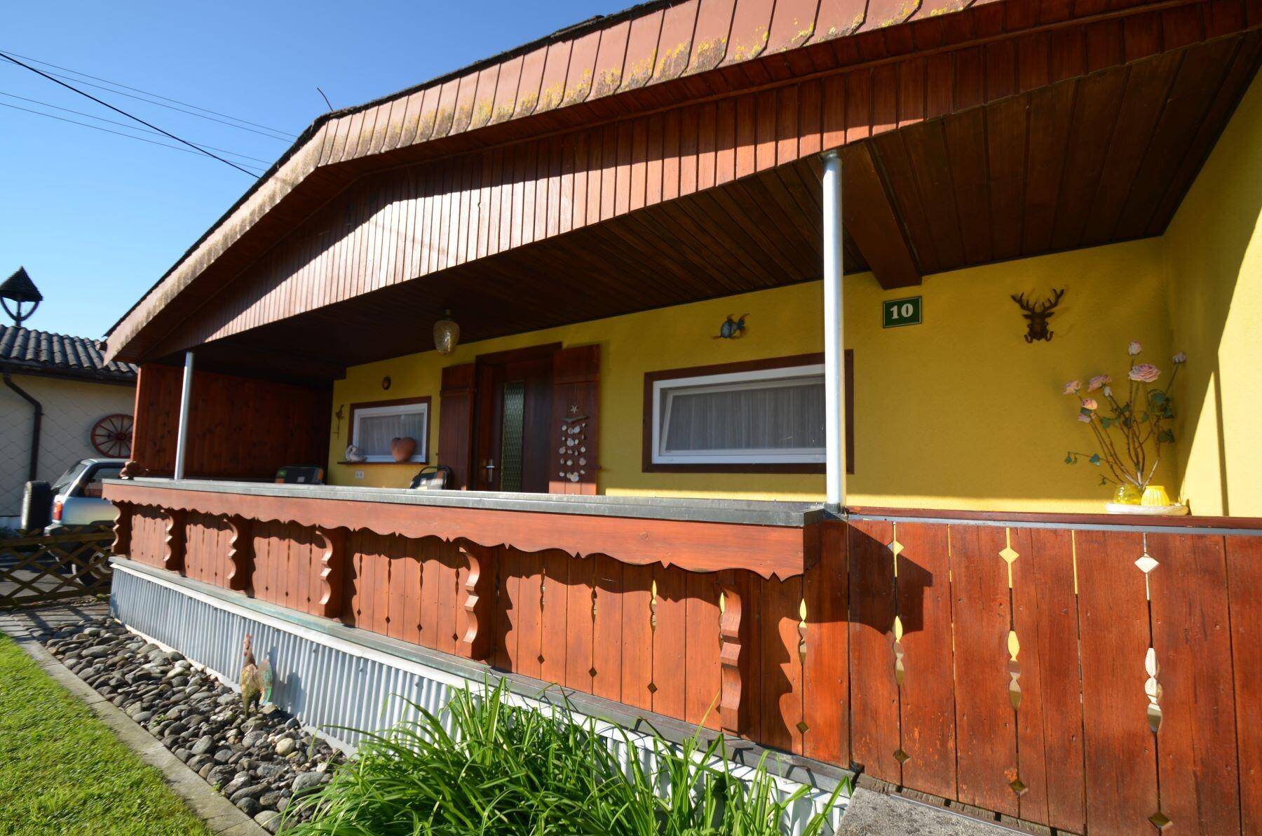 Nahaufnahme der gelben Hausfassade mit überdachtem Eingangsbereich und Holzbalkon.