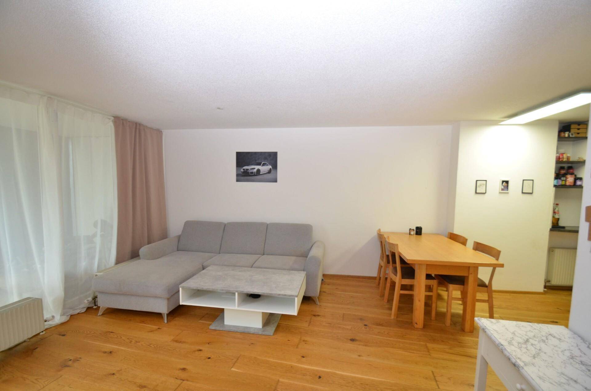 Heller Wohn- und Essbereich mit Holzboden, beigem Sofa und Esstisch für vier Personen.