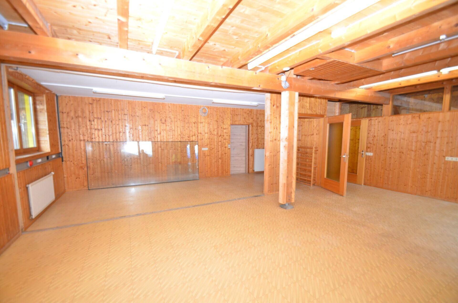 Großer, leerer Gewerberaum mit Holzverkleidung, Holzbalkendecke und Linoleumboden, bereit zur individuellen Gestaltung.