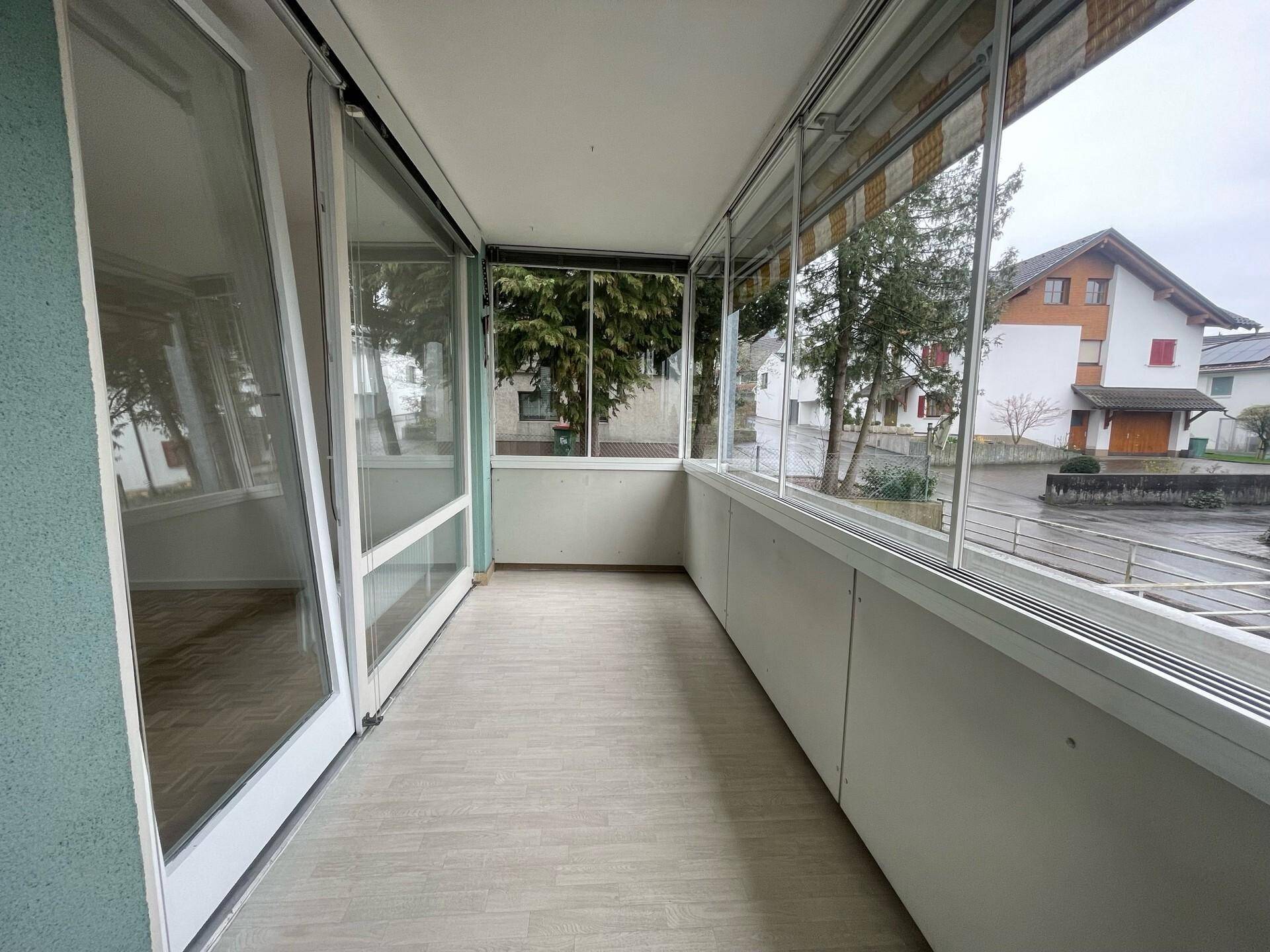 Verglaster Balkon mit Fliesenboden und Blick auf die umliegenden Häuser und Bäume.