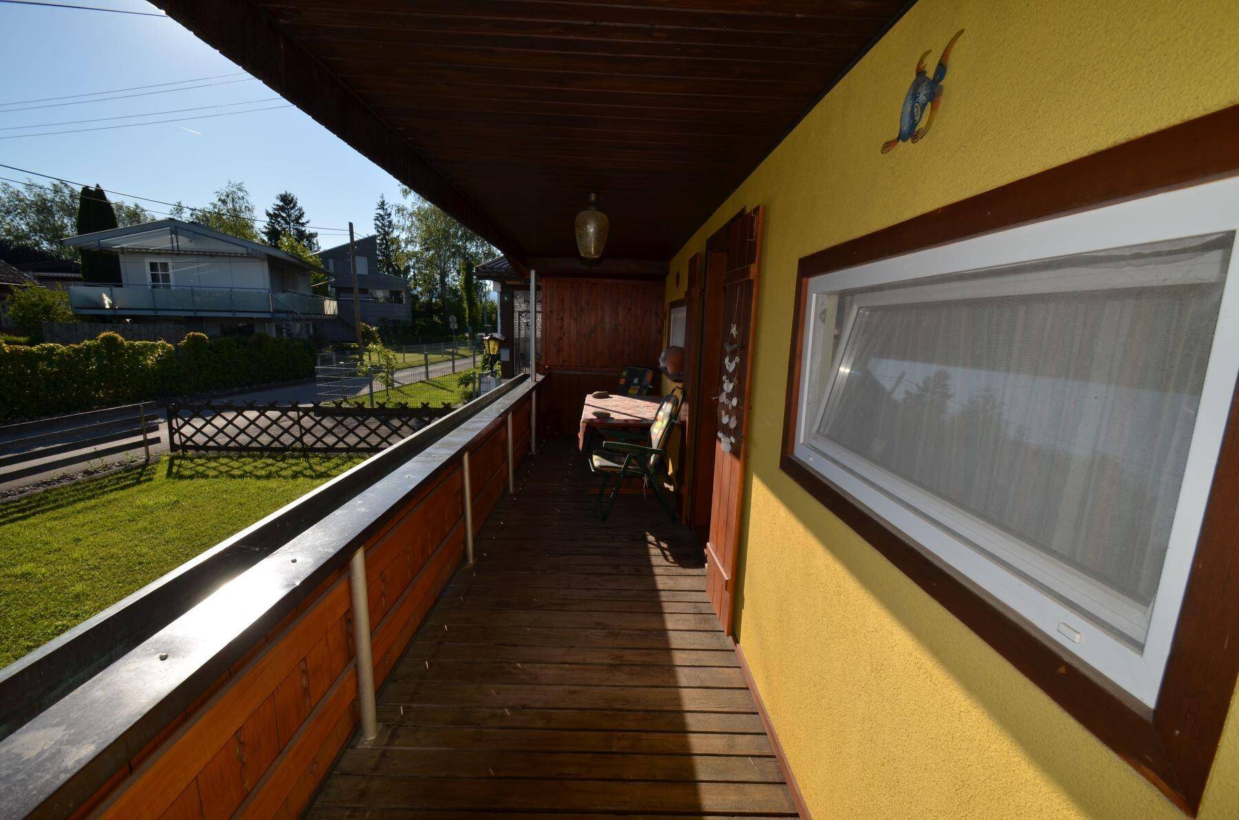 Überdachter Holzbalkon mit Blick auf die grüne Umgebung und die ruhige Wohnstraße.