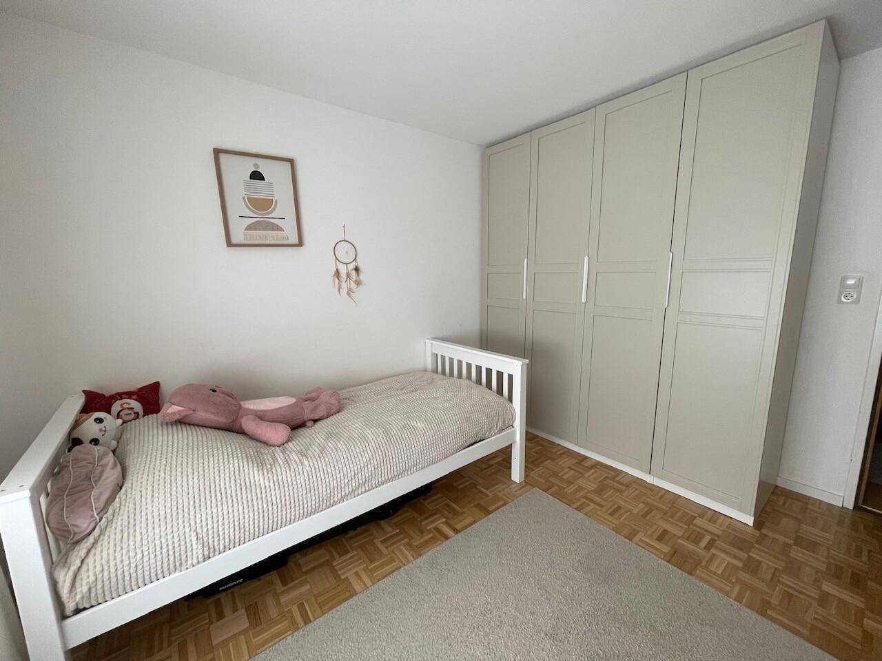 Freundliches Kinderzimmer mit weißem Bett, großem Kleiderschrank und Parkettboden, bietet viel Stauraum.