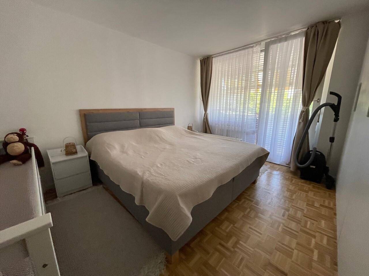 Gemütliches Schlafzimmer mit großem Doppelbett, Parkettboden und Fenster mit Vorhängen für angenehme Lichtverhältnisse.