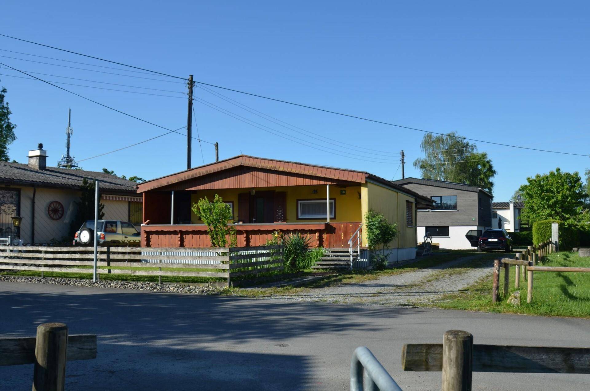 Blick auf das Haus von der Straße, umgeben von weiteren Wohnhäusern und viel Grün.