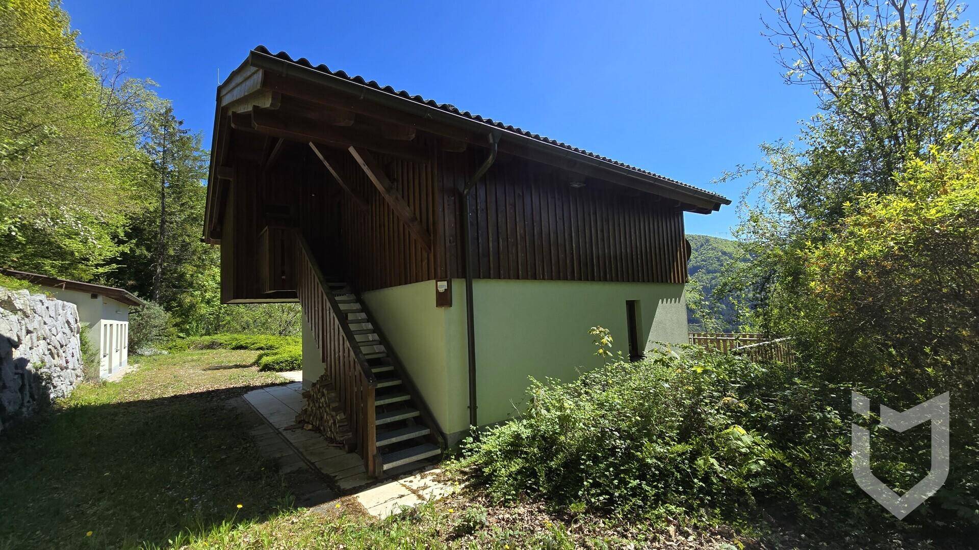 Seitenansicht des Hauses mit Außentreppe aus Holz, die zum oberen Stockwerk und Balkon führt.