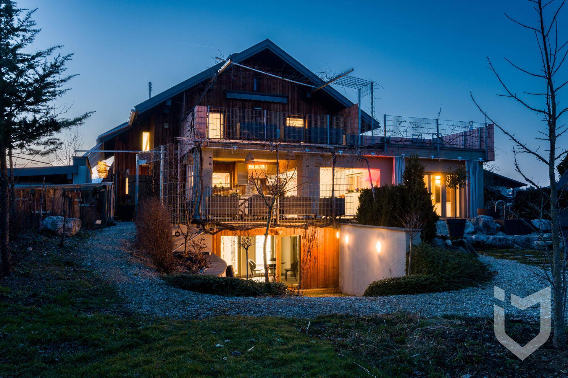 Charmantes Holzhaus bei Dämmerung mit beleuchteten Innenräumen und Außenbereichen.