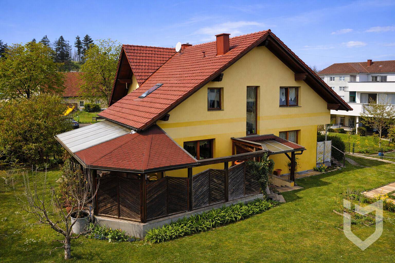 Luftaufnahme eines gepflegten gelben Hauses mit rotem Ziegeldach und weitläufigem grünen Garten.