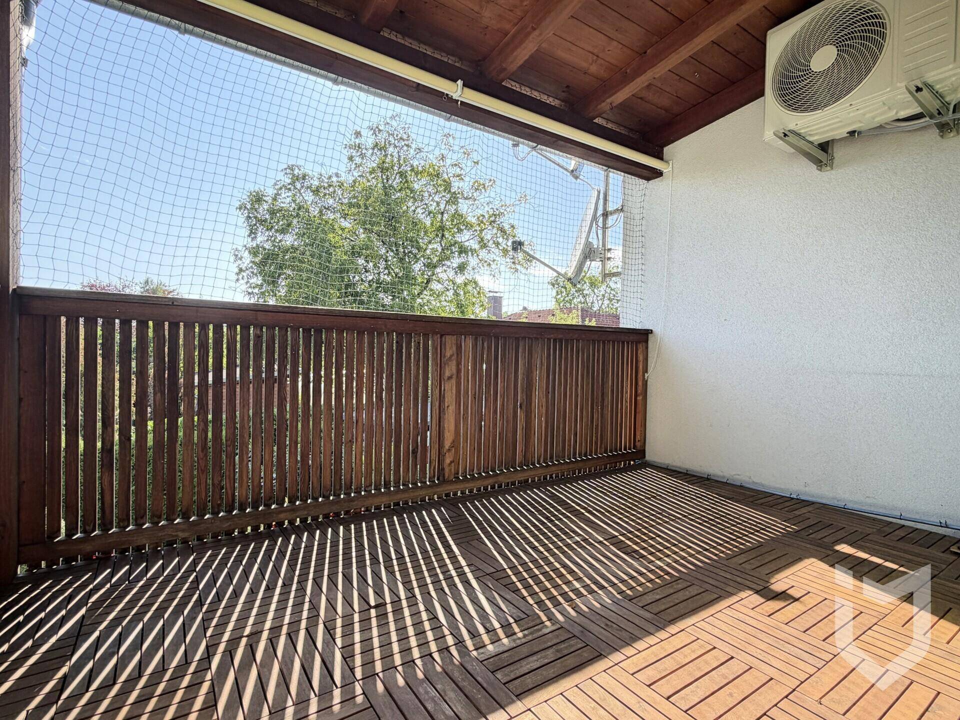 Balkon mit Holzboden, Schutznetz und einer außen angebrachten Klimaanlage.