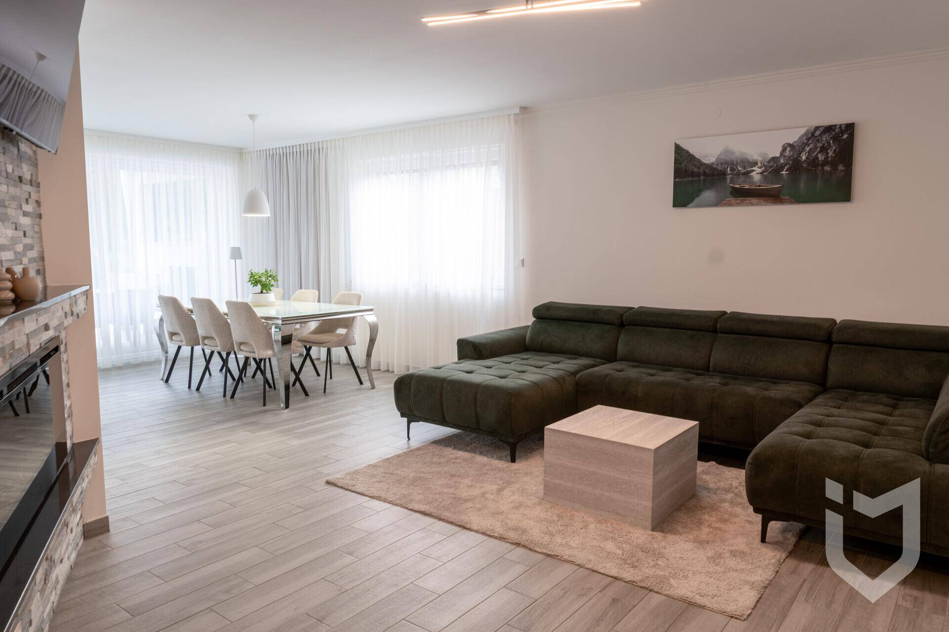 Offener Wohn-Essbereich mit großem Sofa, Esstisch und viel Tageslicht durch Fenster.