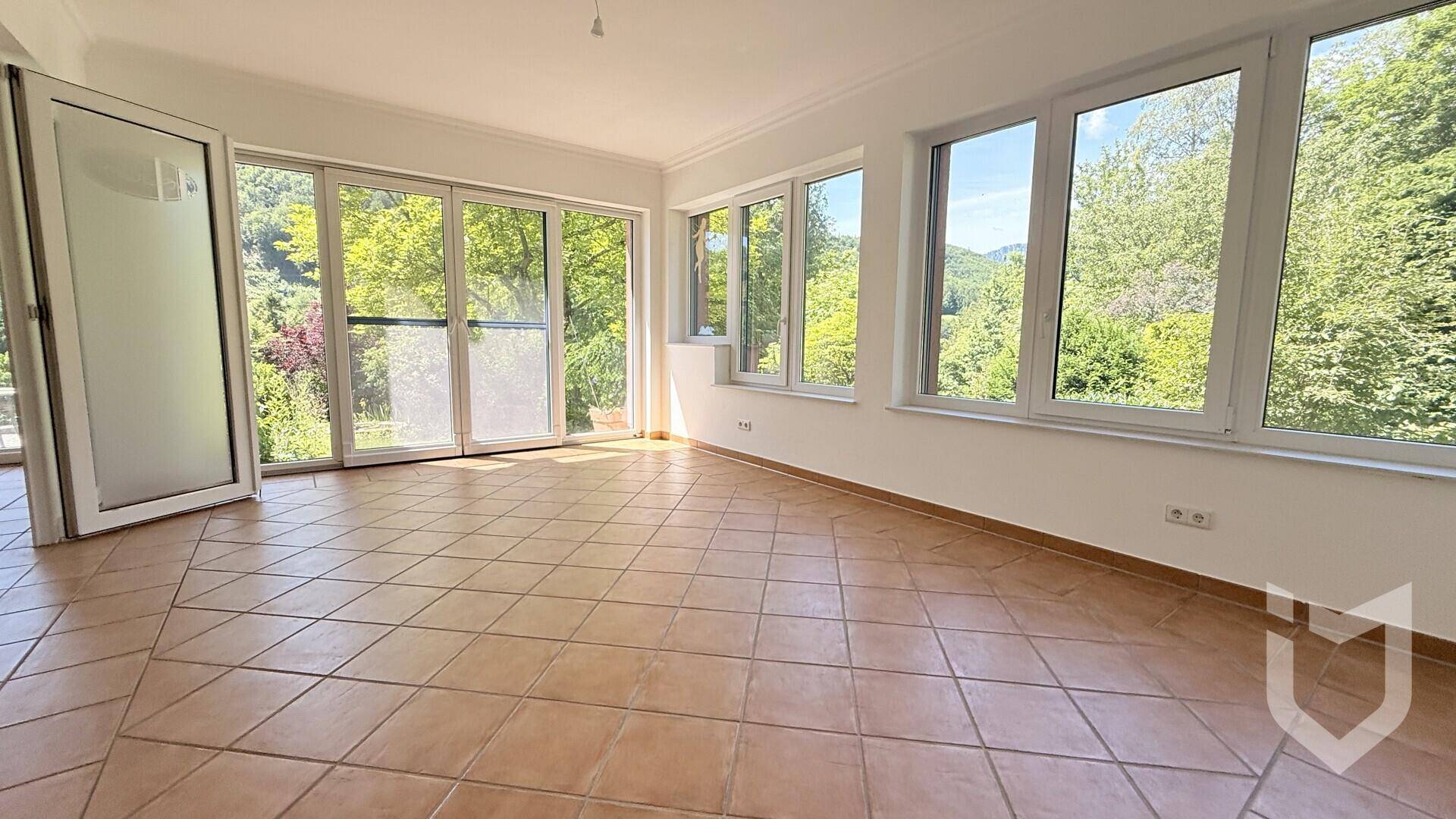 Heller Wohnraum mit Terrakotta-Fliesenboden und großen Glasfronten mit Blick ins Grüne.
