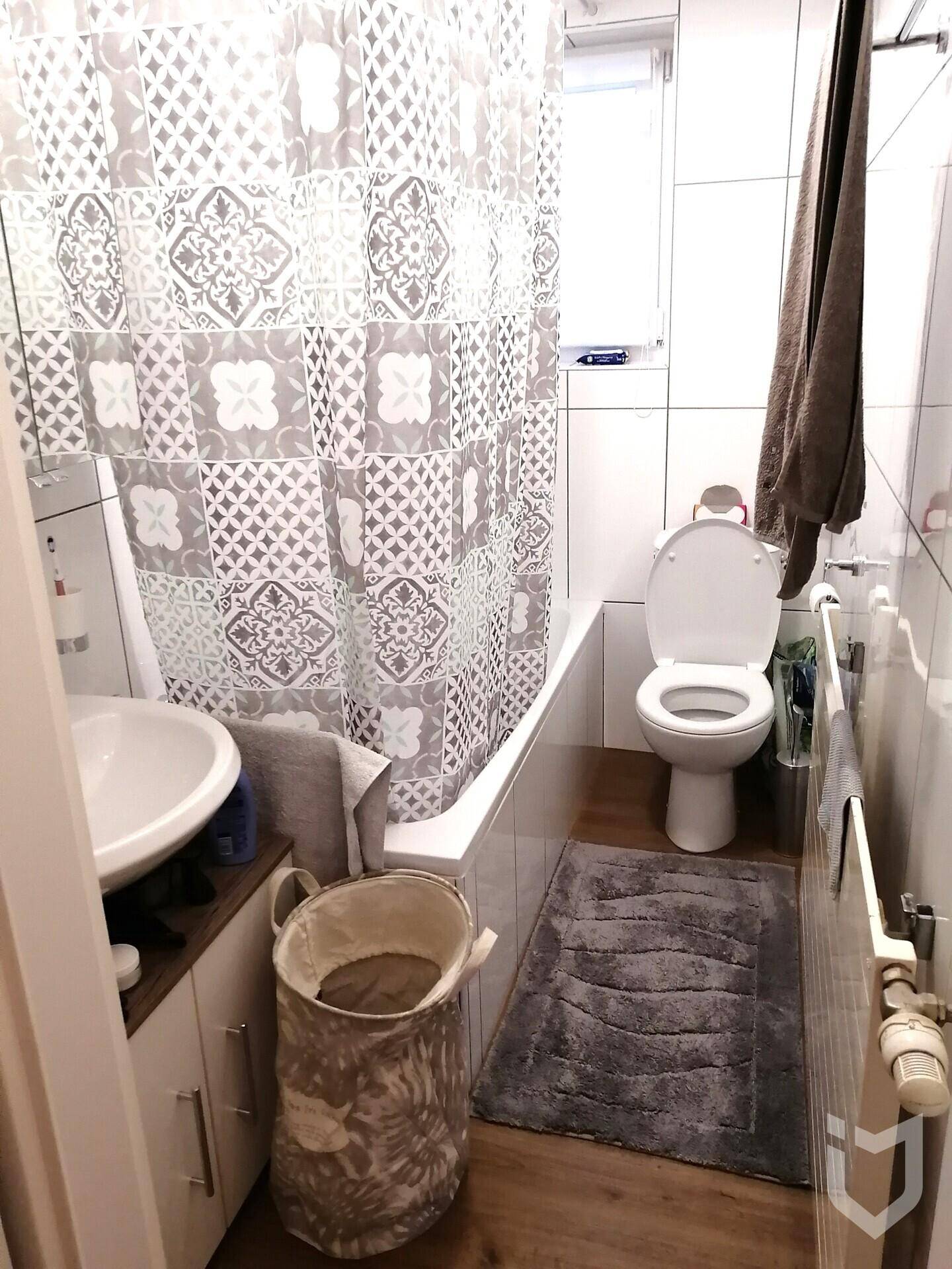 Badezimmer mit Badewanne, Duschvorhang und modernen Fliesen in Grau-Weiß.