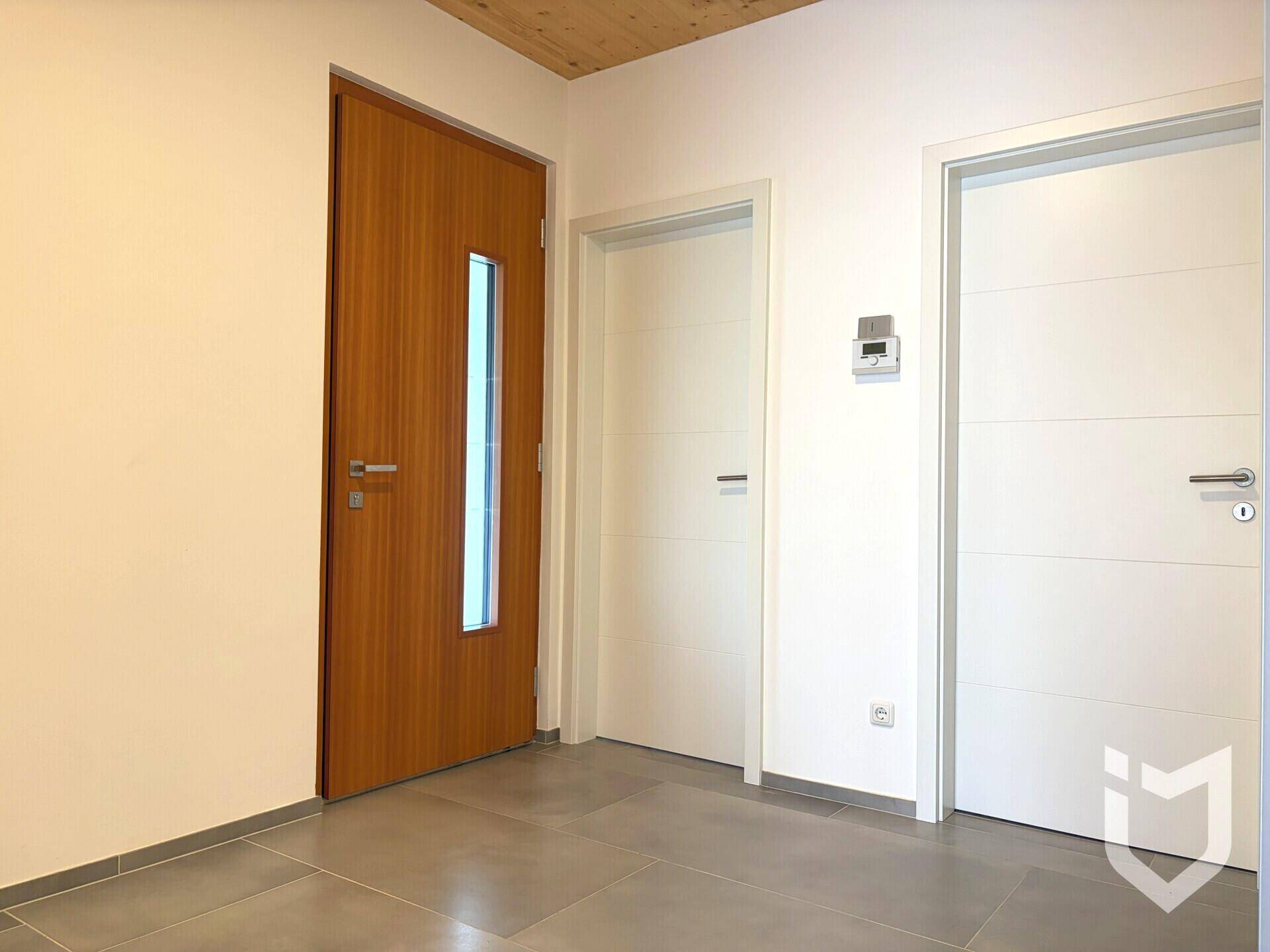 Moderner Eingangsbereich mit grauen Fliesen, einer Holztür mit Glaseinsatz und weißen Innentüren.