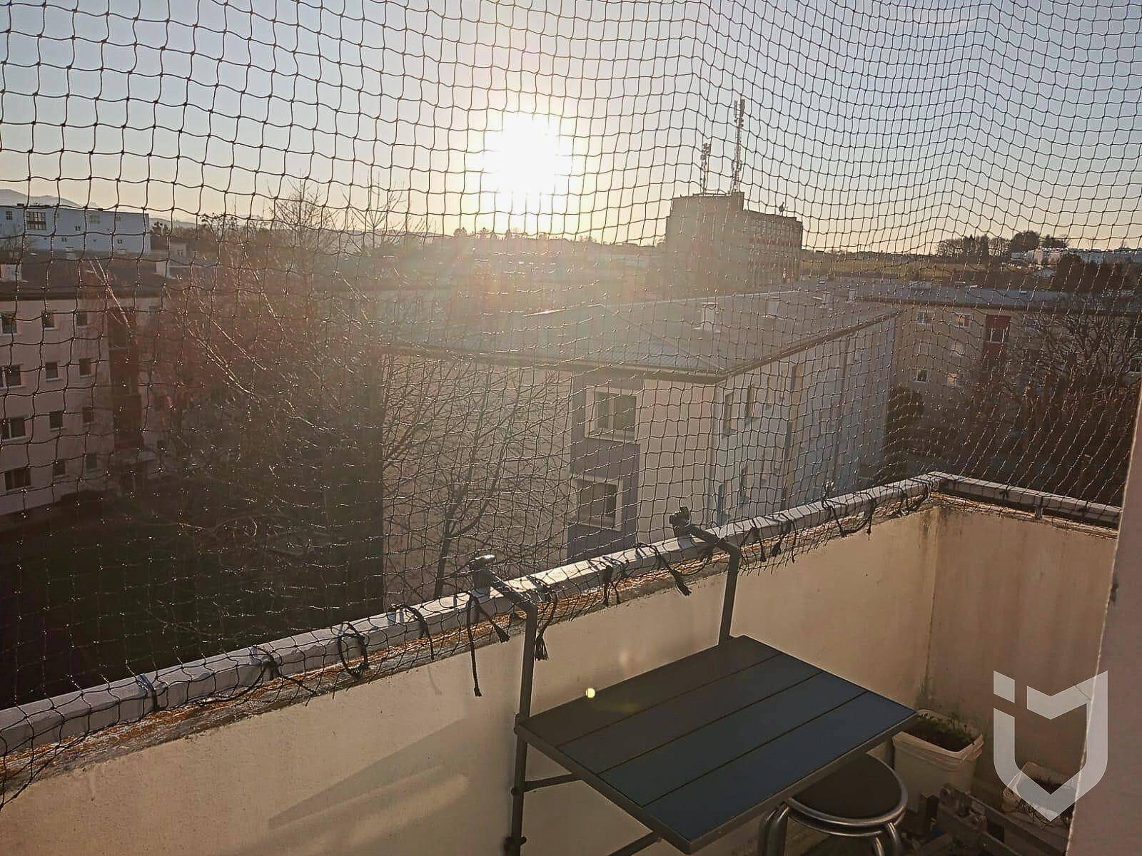 Balkon mit kleinem Tisch und Sicherheitsnetz bei Sonnenuntergang über der Stadt.