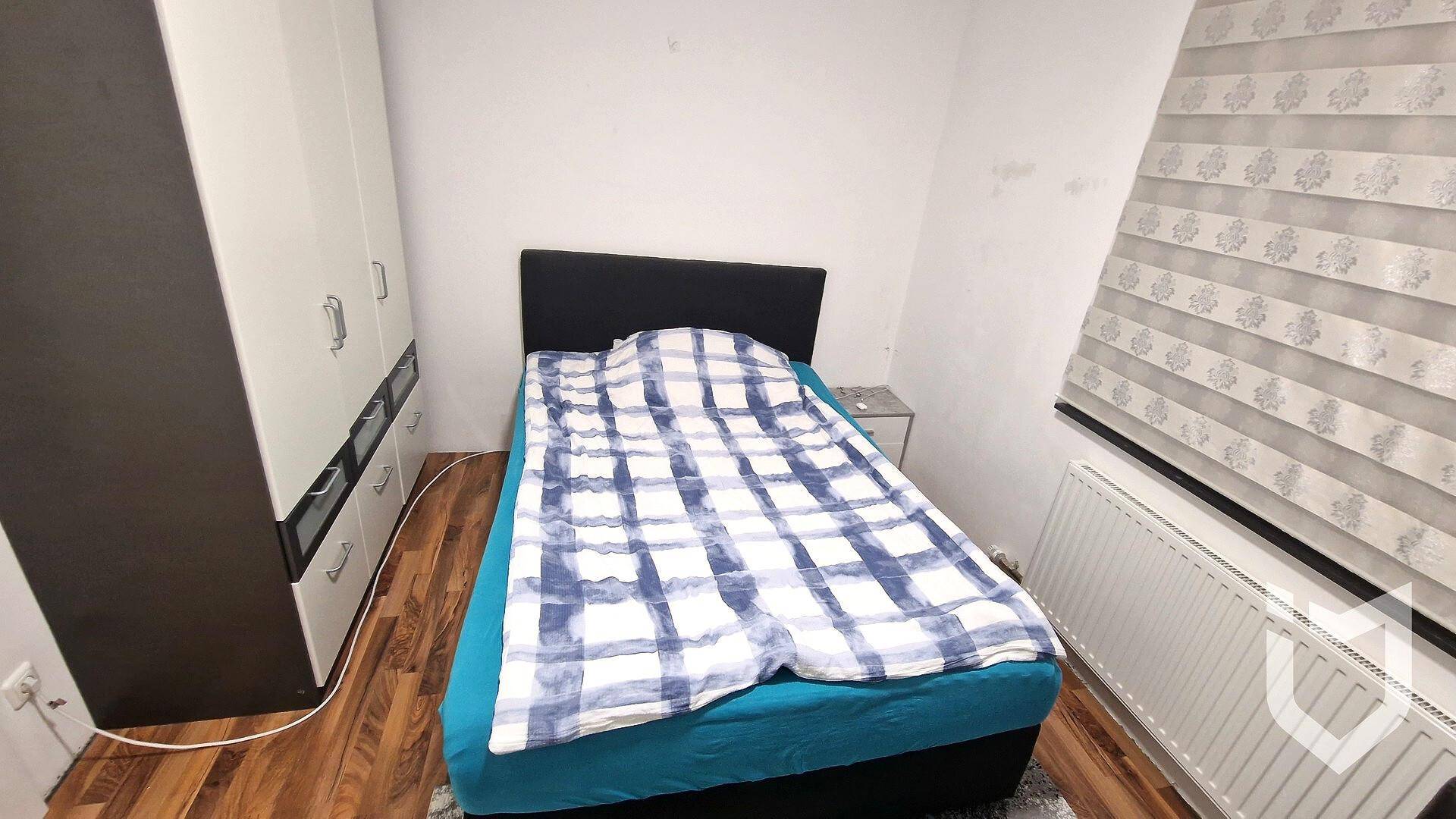 Schlafzimmer mit Einzelbett, Kleiderschrank und Fenster mit Jalousien.