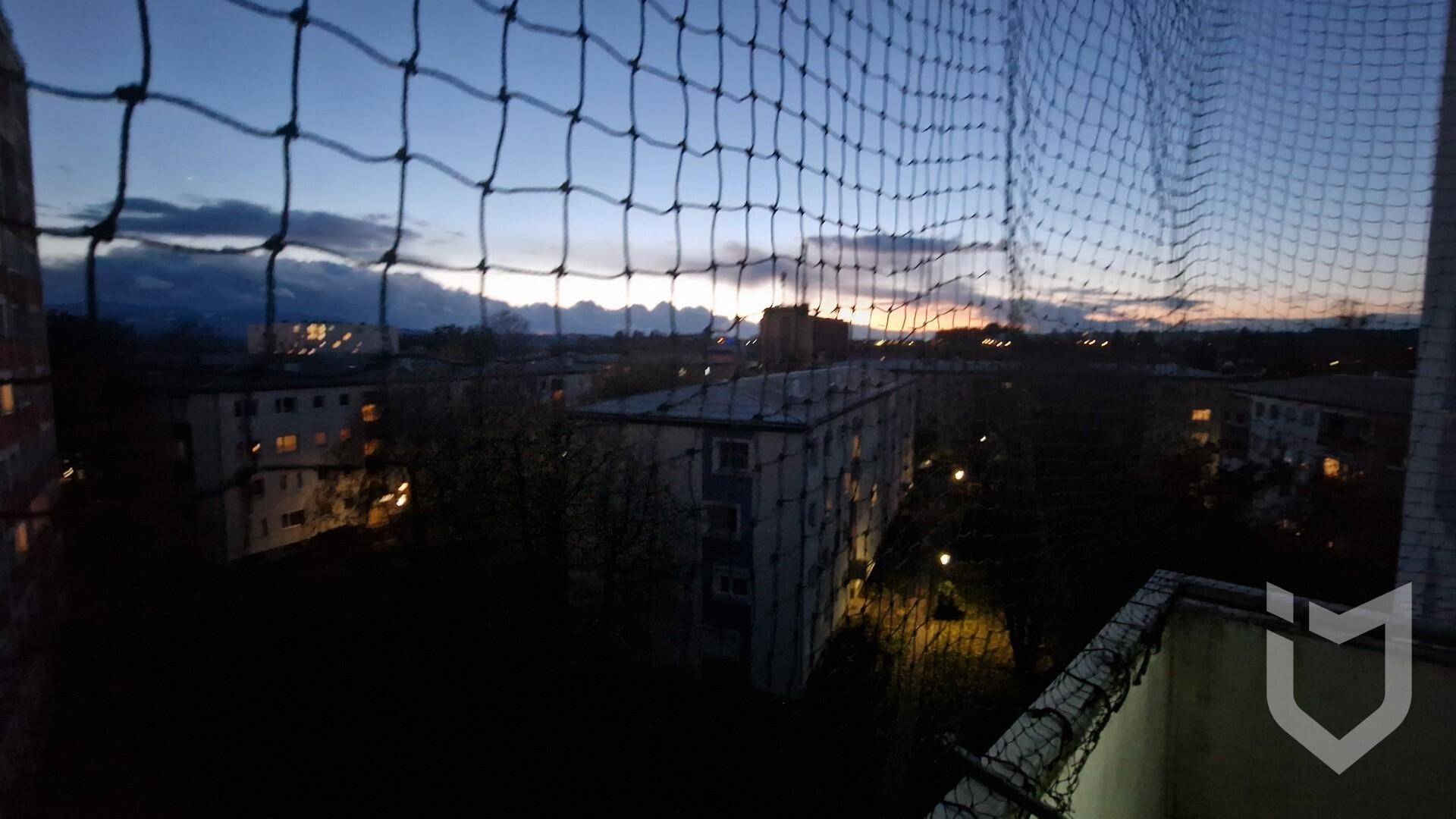Balkonblick bei Dämmerung mit Sicherheitsnetz und Lichtern der Stadt im Hintergrund.