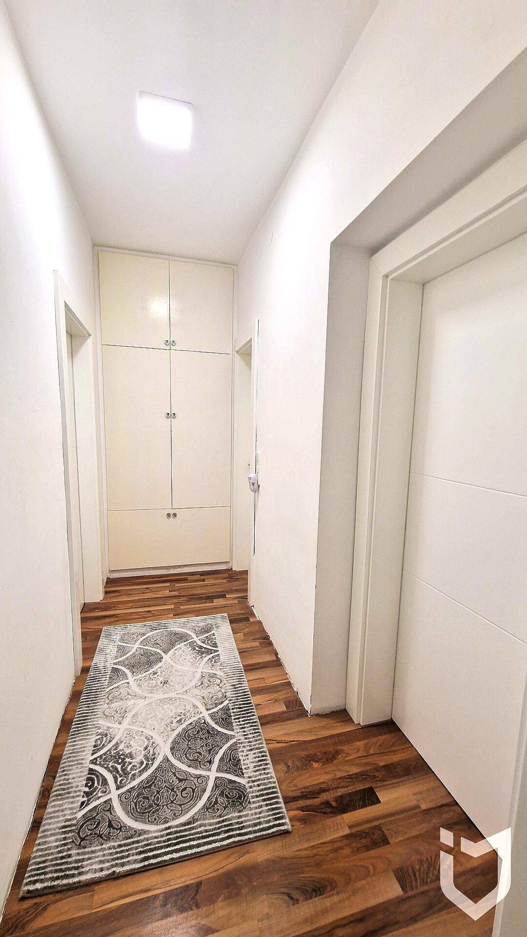 Heller Flur mit Einbauschränken am Ende und gemustertem Teppich auf Holzboden.