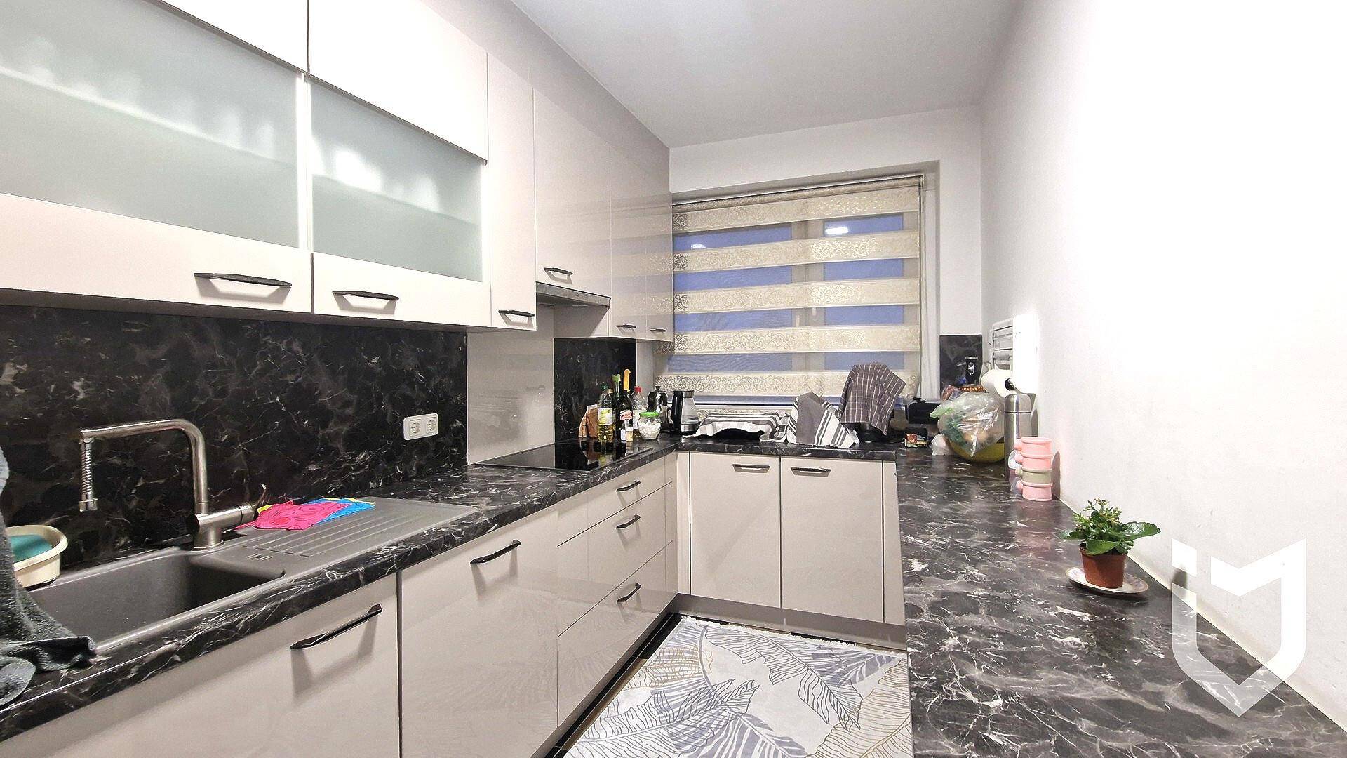 Moderne Küche mit hellgrauen Schränken, dunklen Arbeitsplatten und Fenster mit Jalousien.