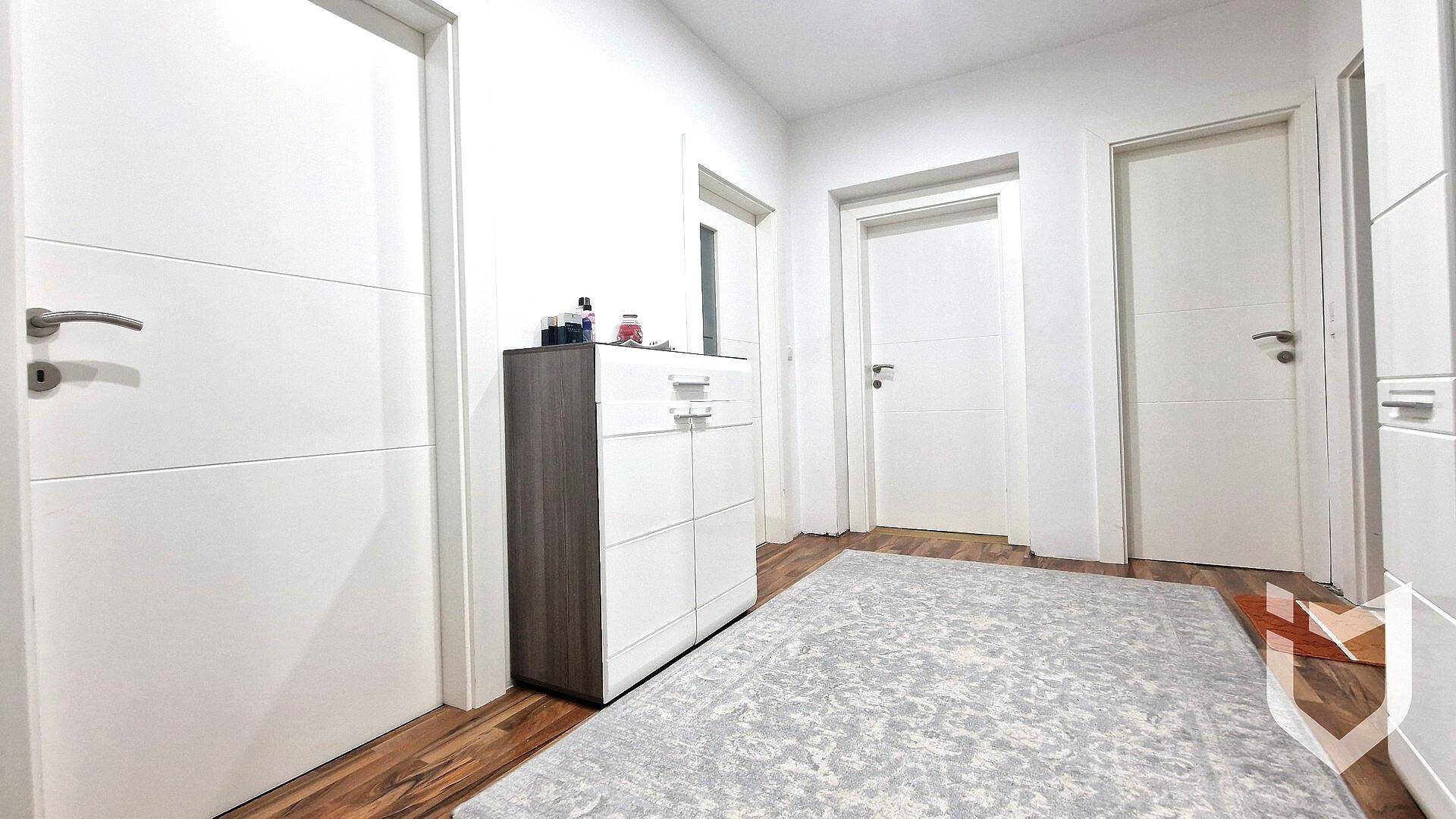 Heller Flur mit mehreren weißen Türen, einem Schuhschrank und gemustertem Teppich.