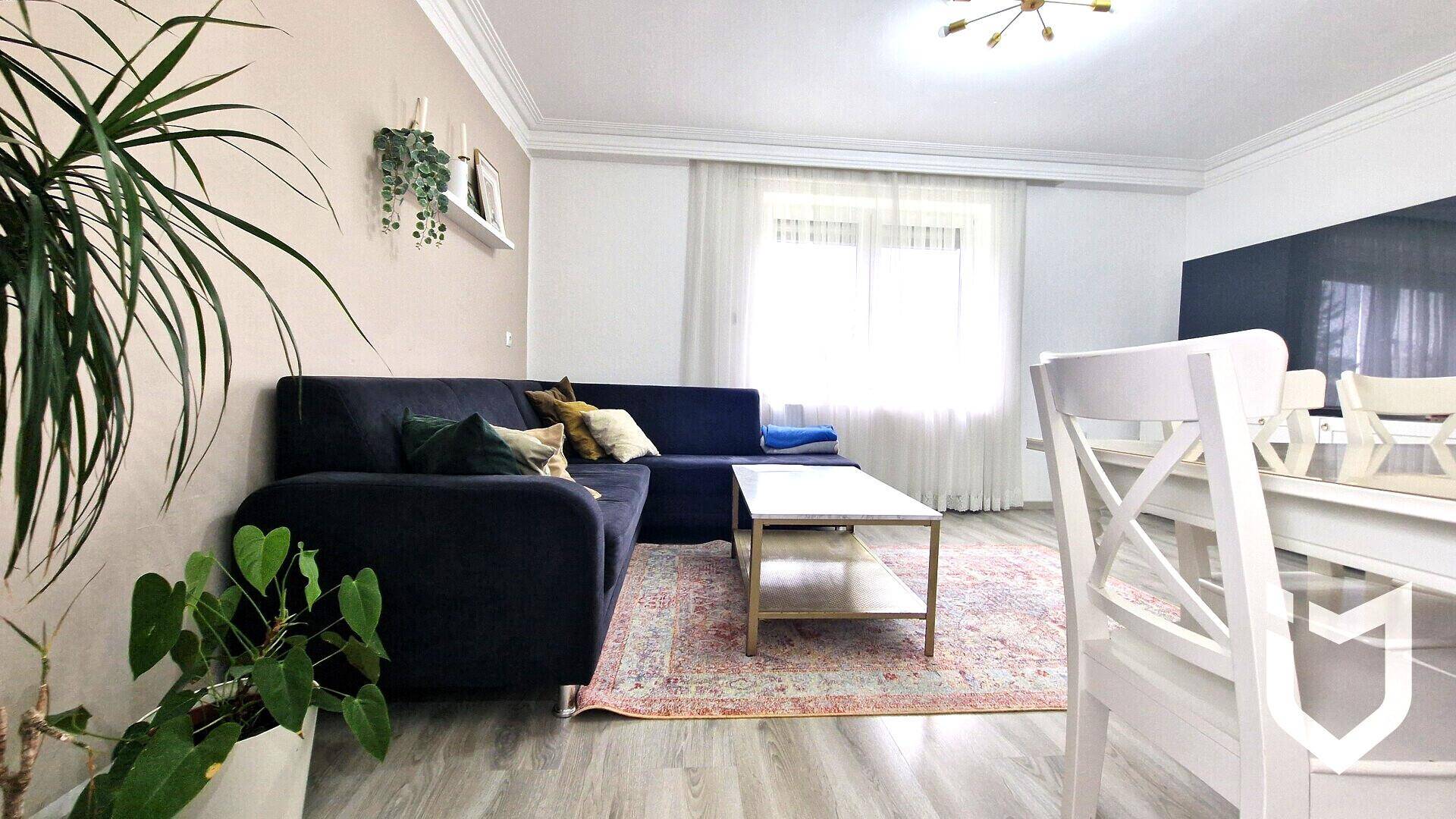 Gemütlicher Wohn-Essbereich mit dunklem Sofa, Couchtisch und hellem Laminatboden.