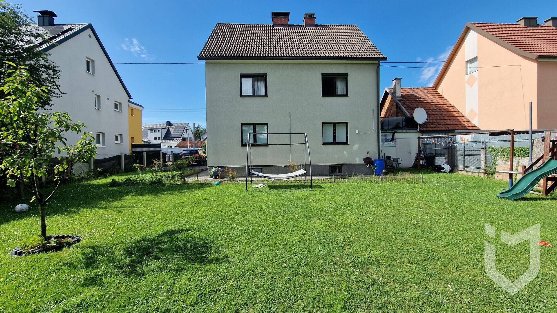 Hinteransicht des Hauses mit weitläufigem Rasen, Schaukel und Rutsche im Gartenbereich.