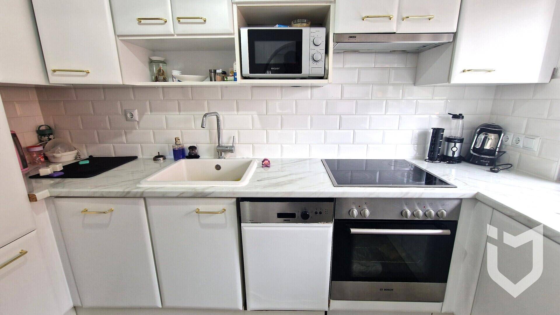 Moderne Einbauküche mit weißen Schränken, Induktionskochfeld und integrierten Geräten.
