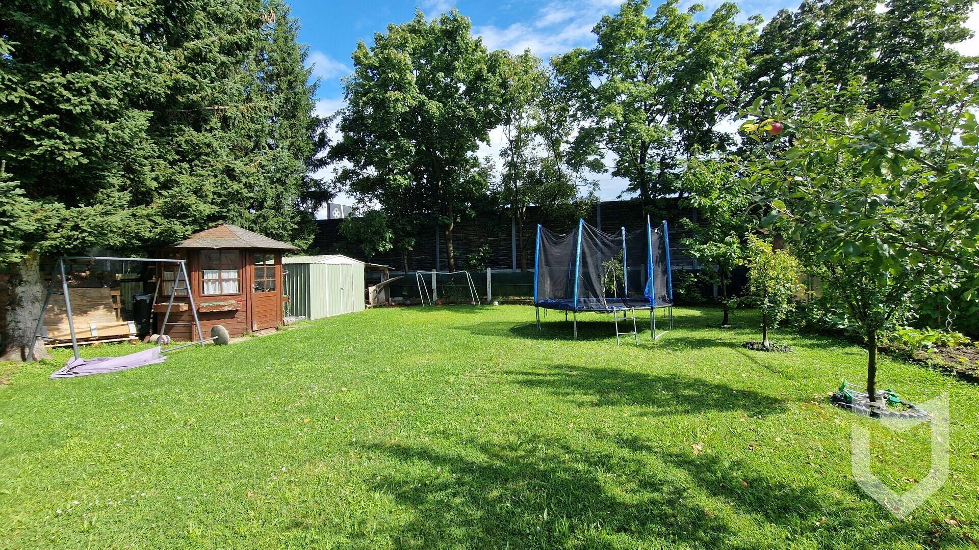 Weitläufiger Garten mit altem Baumbestand, Trampolin, Spielgeräten und Gartenhaus.