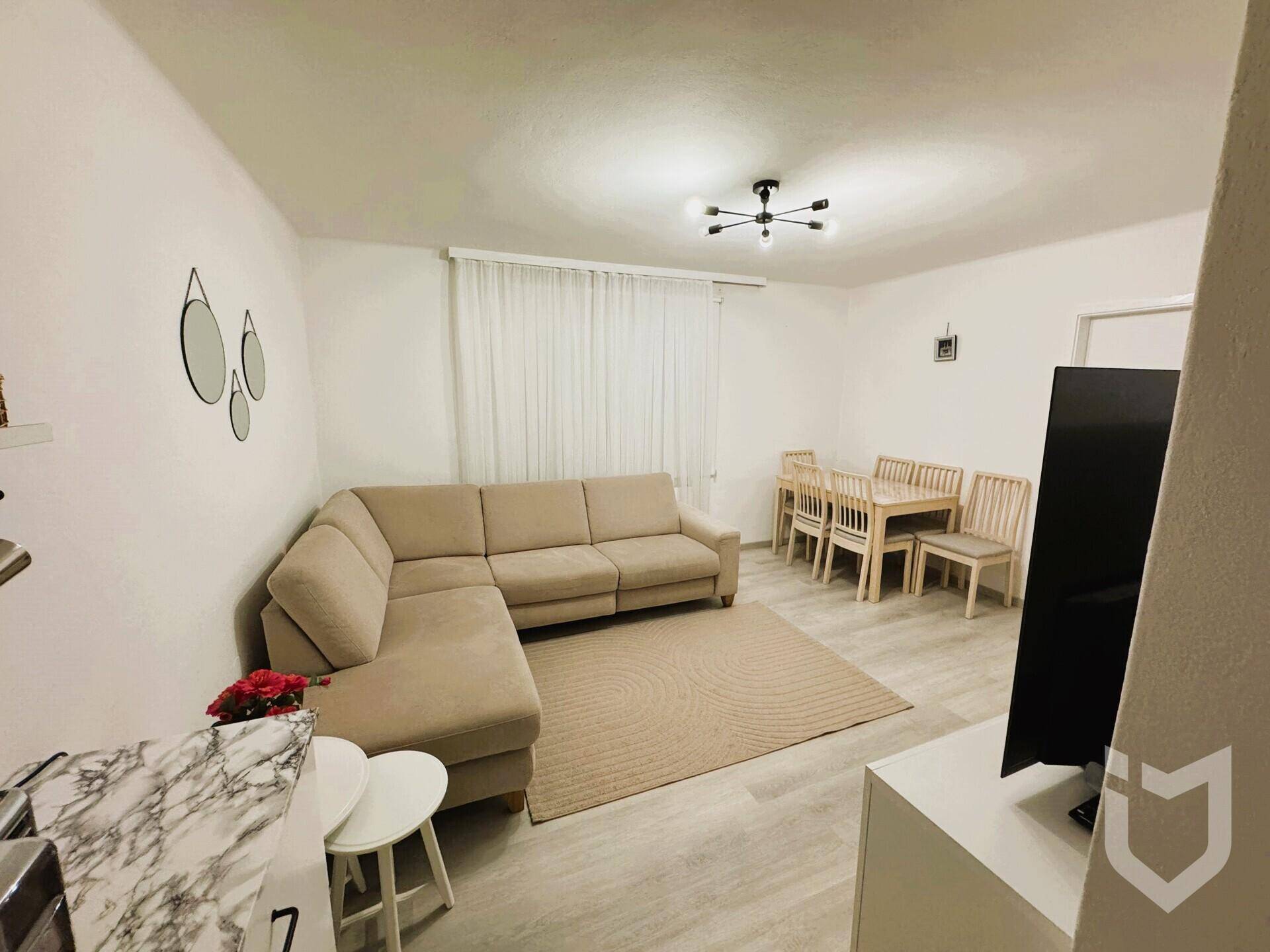 Geräumiger Wohn-Essbereich mit beigem Ecksofa, Esstisch und hellem Laminatboden.