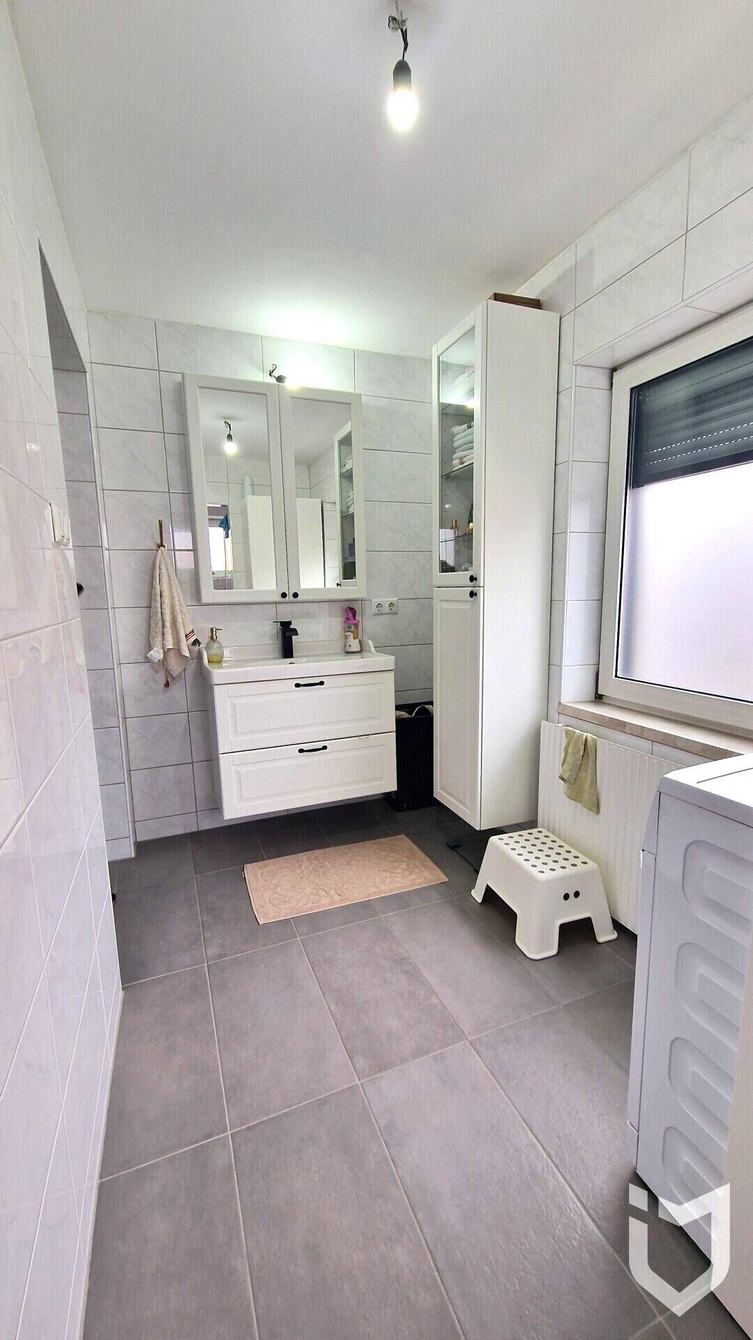 Helles Badezimmer mit modernem Waschtisch, Spiegelschrank und Fenster für Tageslicht.