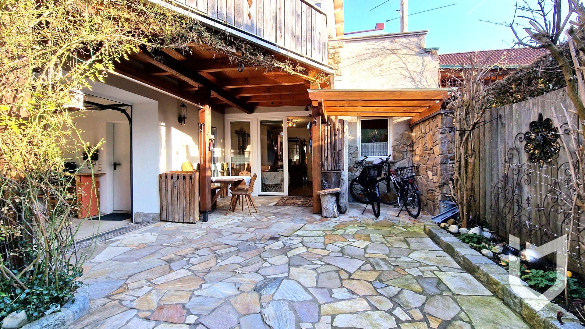 Außenbereich mit Steinboden, überdachter Terrasse und viel Grün.