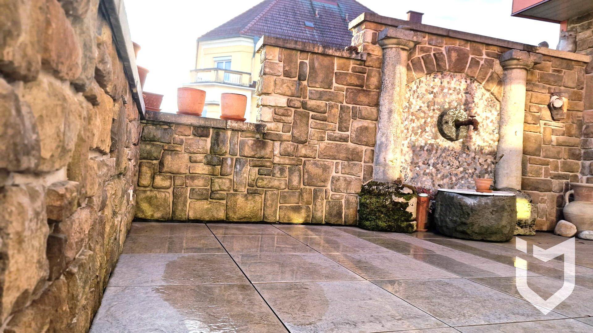 Geräumige Steinterrasse mit hoher Steinmauer und rustikalem Brunnen.