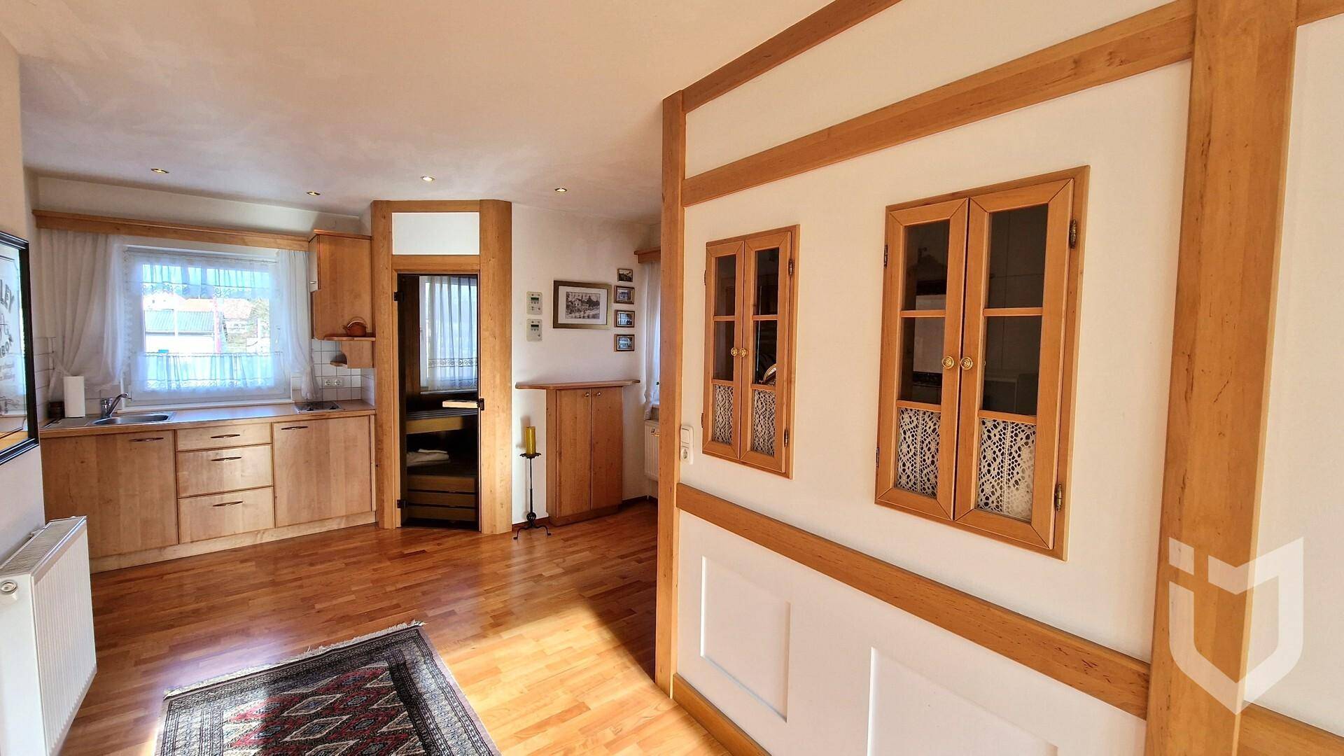 Helle Küche mit Holzschränken, Holzboden und Fenster, offen zum Wohnbereich.