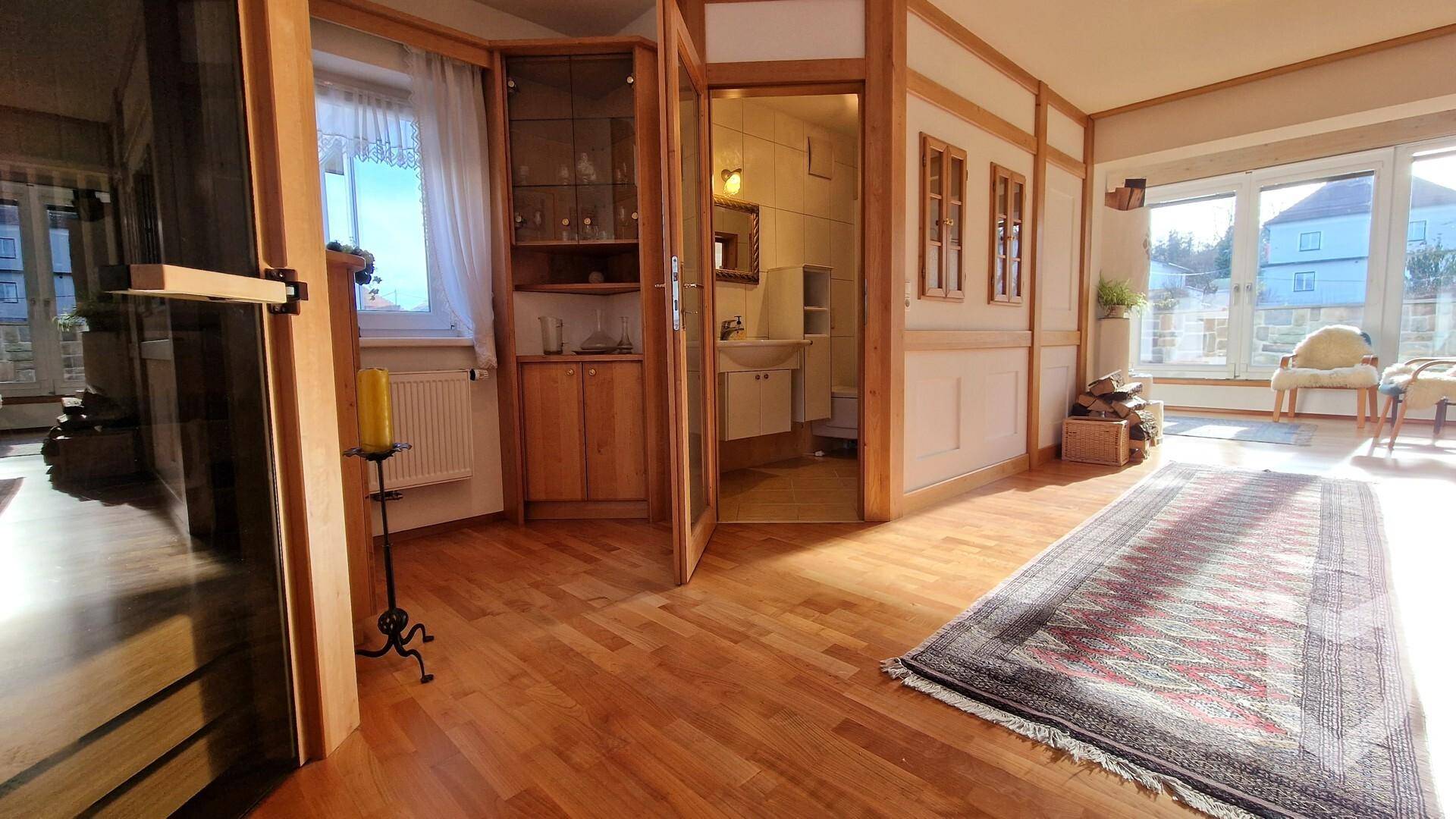 Offener Wohnbereich mit Holzboden, Zugang zu einem Badezimmer und großen Fenstern.