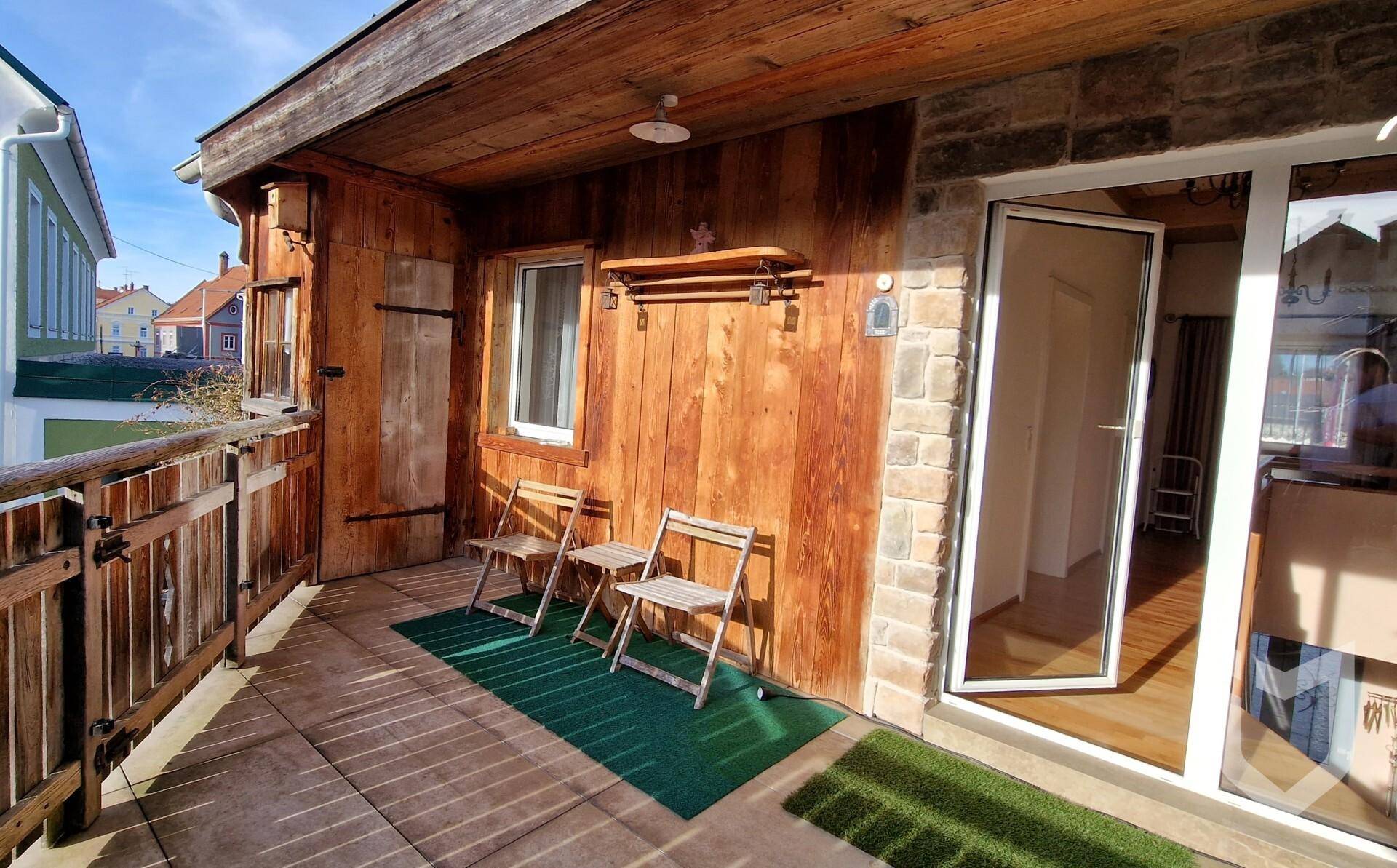 Sonniger Holzbalkon mit Sitzgelegenheiten und Zugang zum Innenbereich.