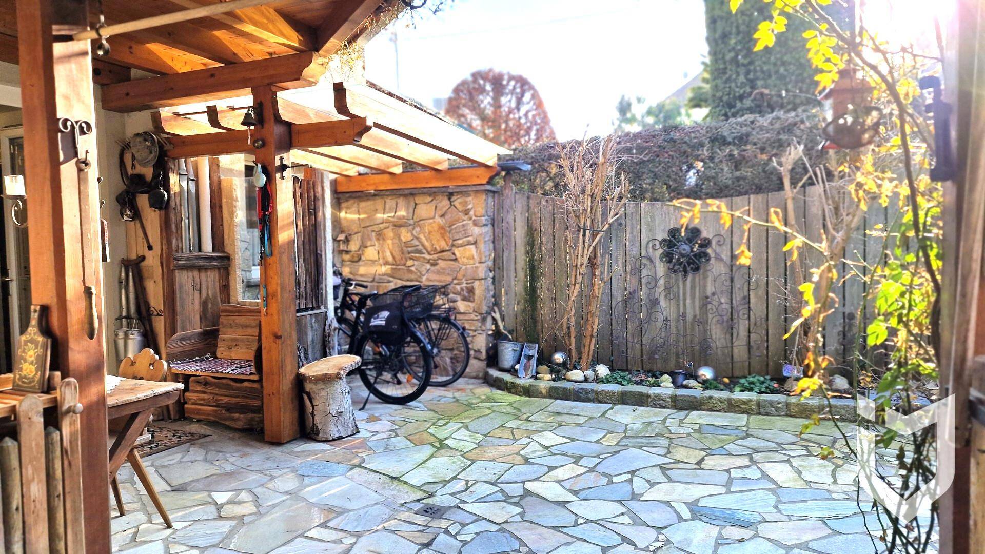 Gemütliche Terrasse mit rustikalem Holzunterstand, Steinboden und dekorativen Elementen.