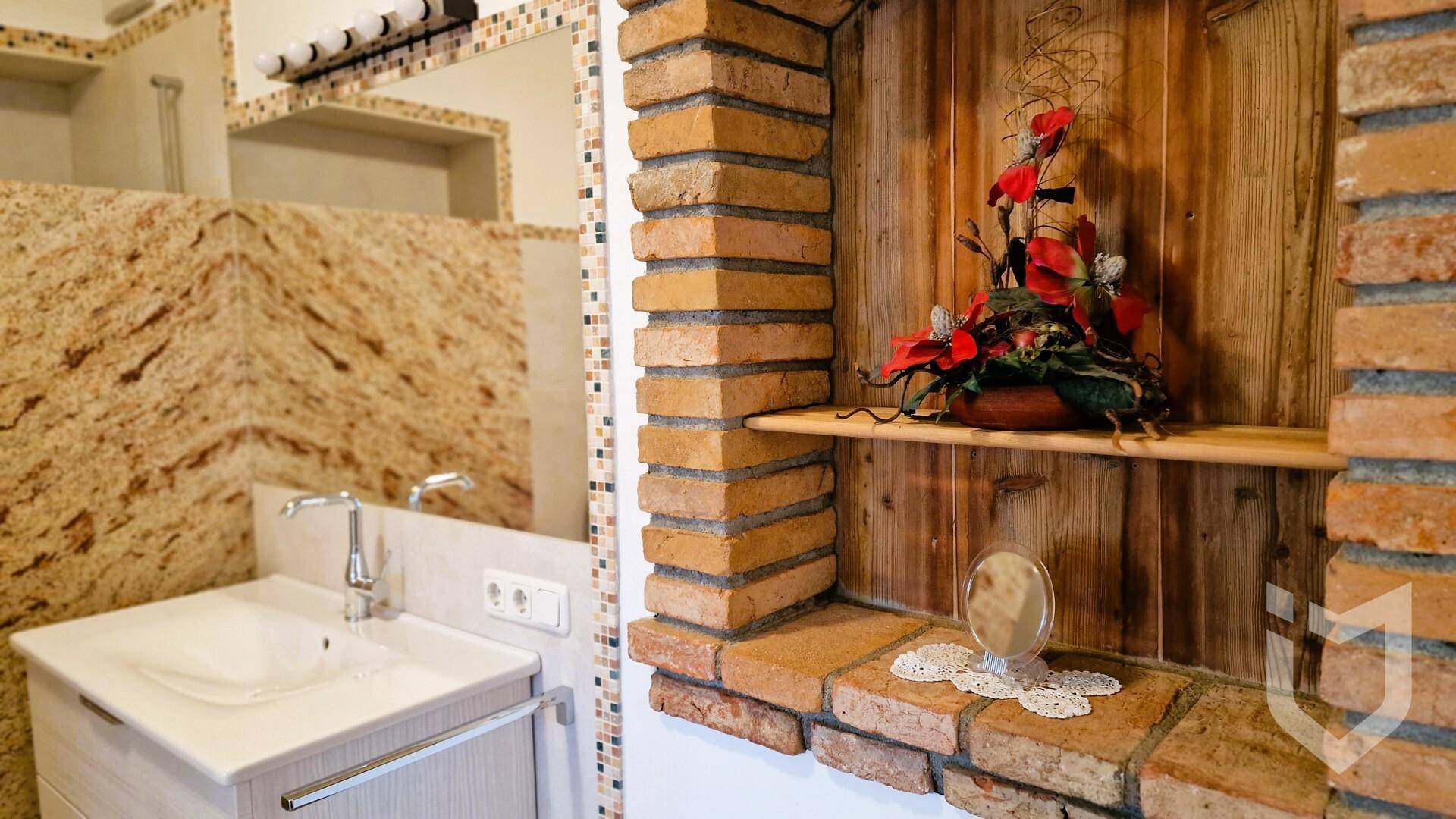 Badezimmer mit Einzelwaschbecken, gemusterten Fliesen und rustikaler Ziegelnische.