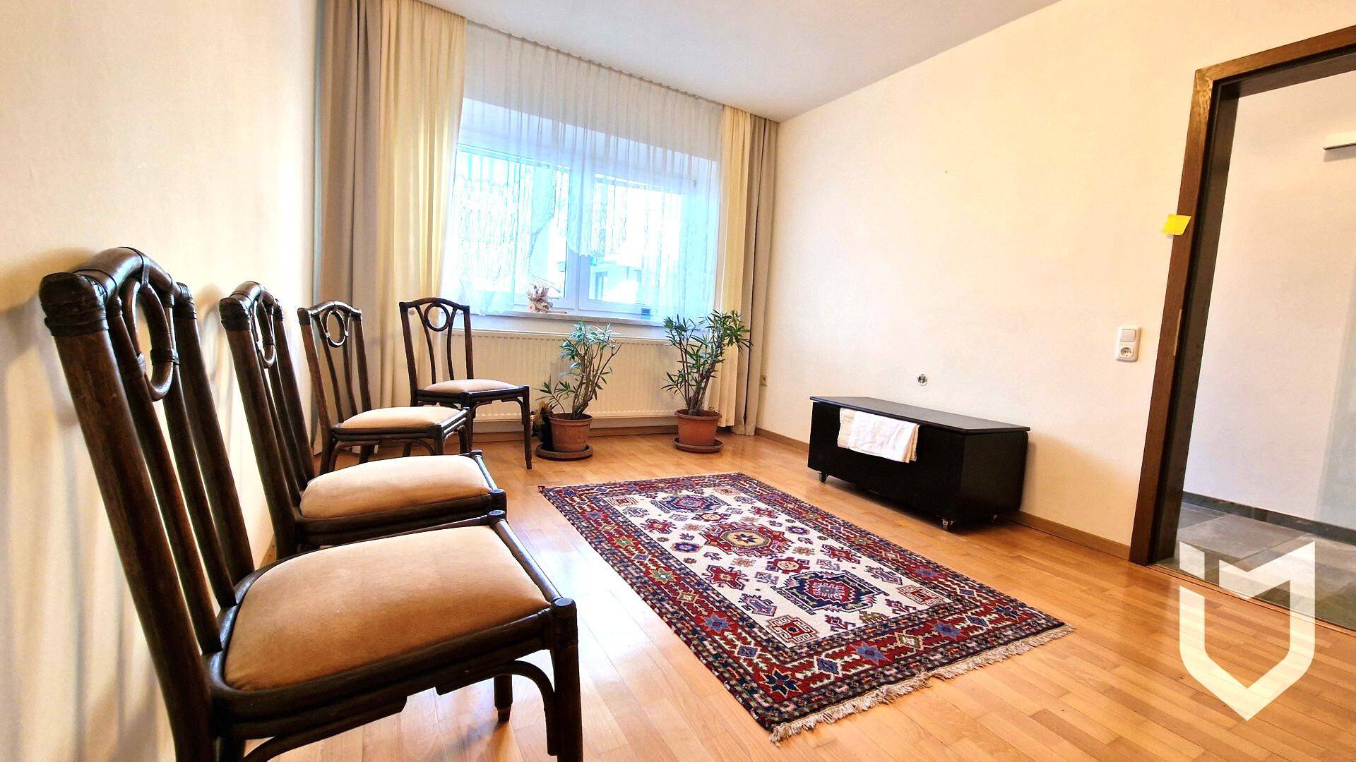 Heller Raum mit Holzboden, Fenster und traditionellen Holzstühlen.