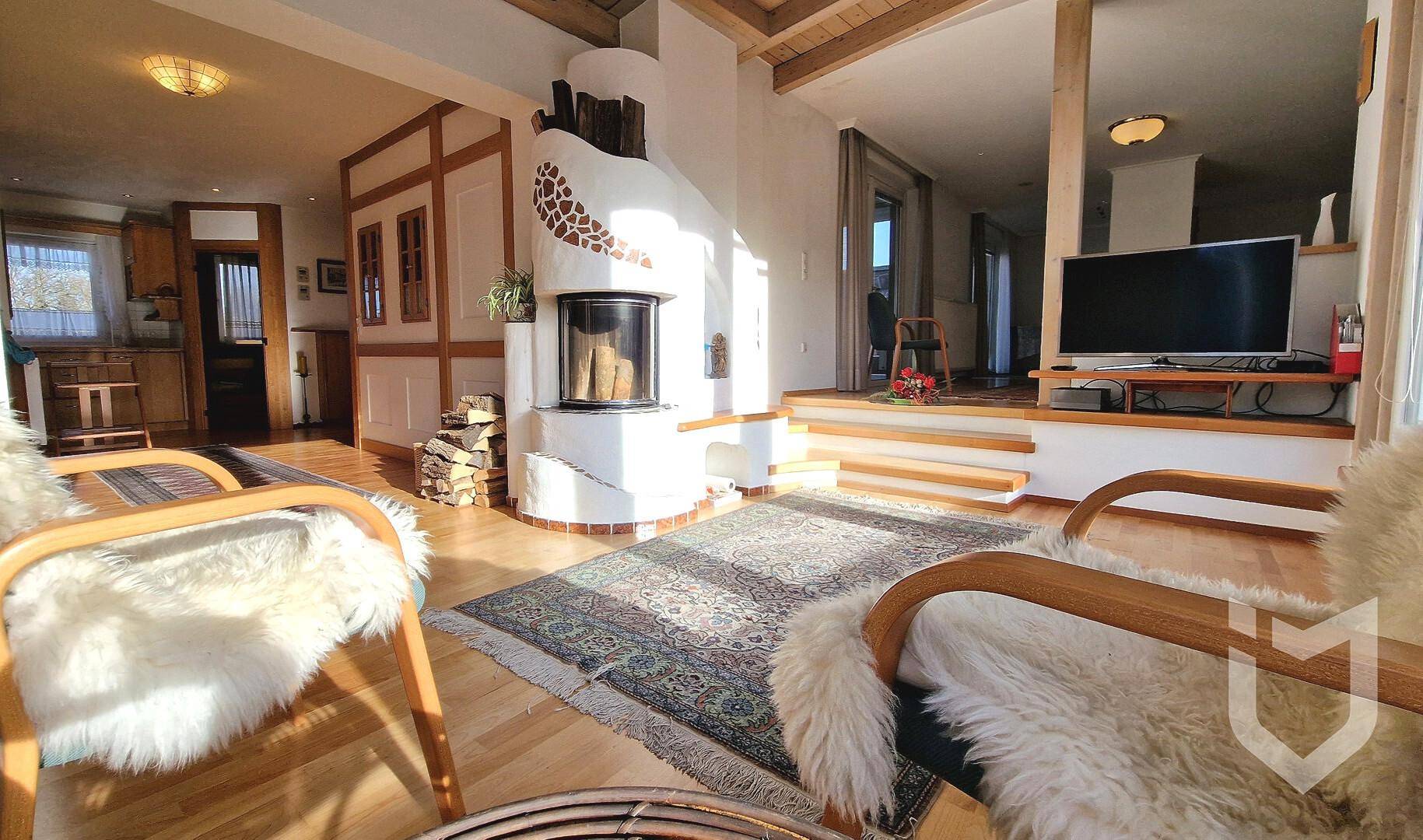 Helles Wohnzimmer mit Kamin, Holzbalkendecke und gemütlichen Sitzgelegenheiten, durchflutet von Sonnenlicht.