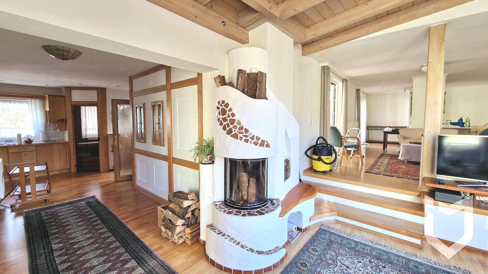 Geräumiges Wohnzimmer mit Kamin, Holzbalkendecke und Übergang zu weiteren Wohnbereichen.