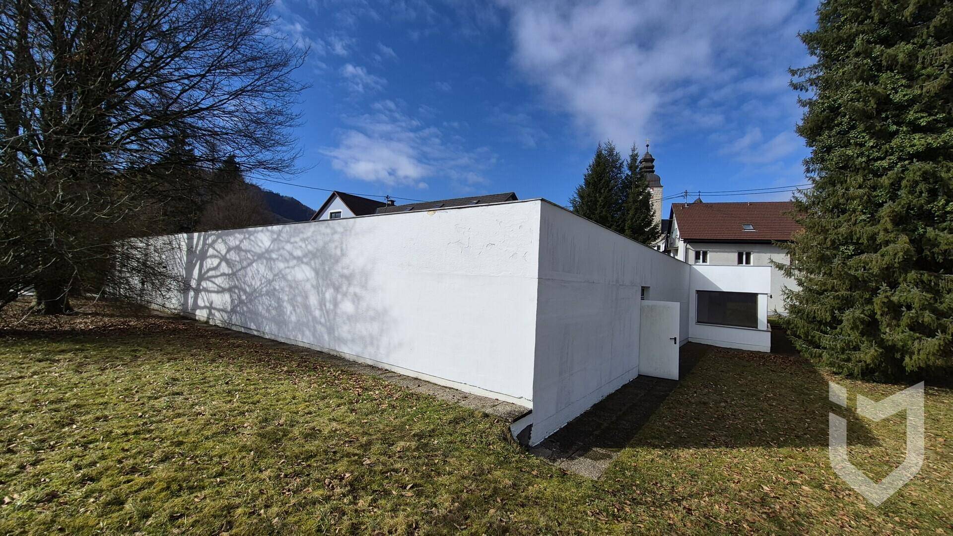 Weitwinkelansicht des weißen Gebäudes mit umliegender Natur und einem Blick auf die Berge.