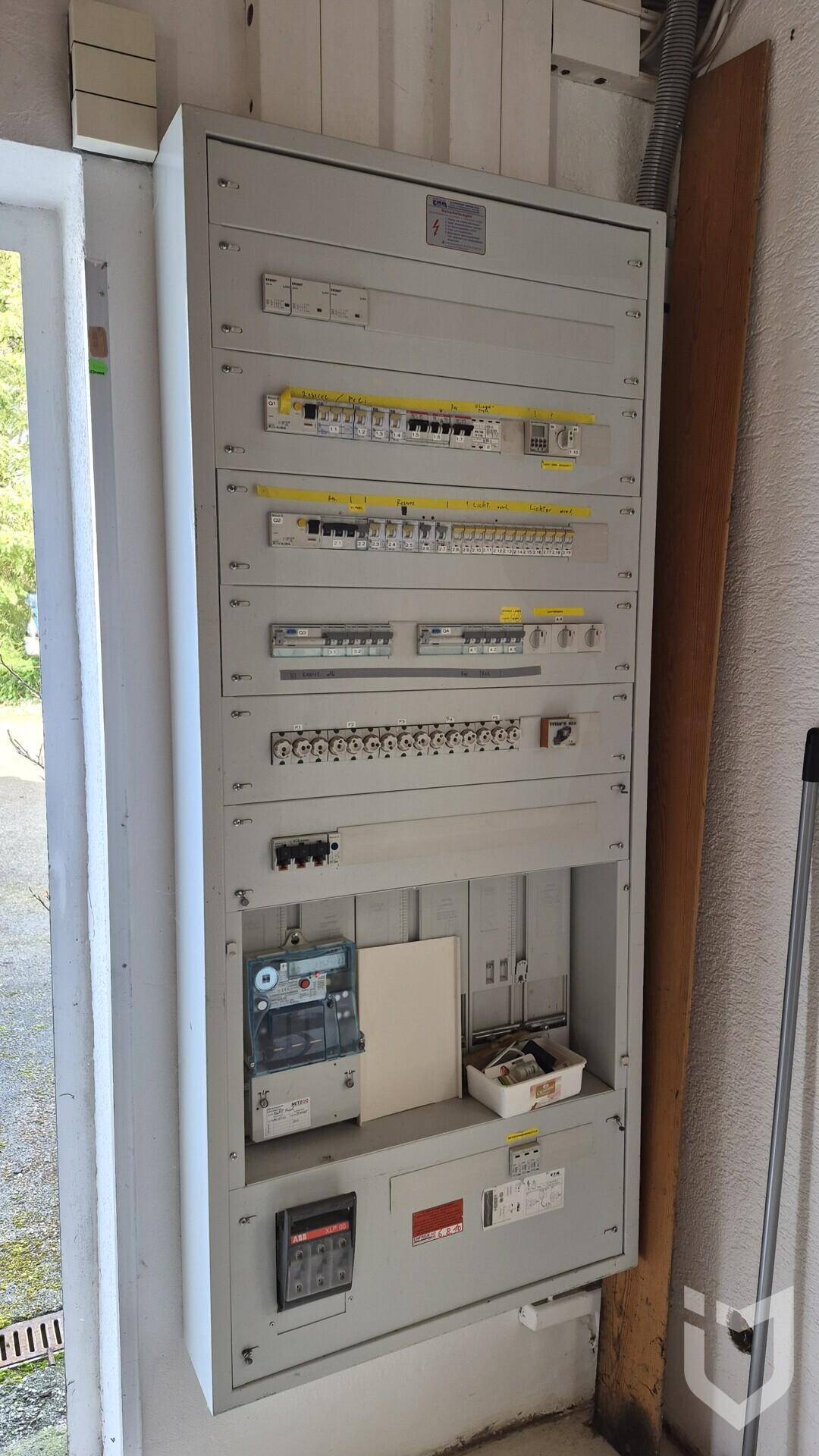 Großer elektrischer Verteilerkasten mit Sicherungen und Zähler in einem Technikraum.