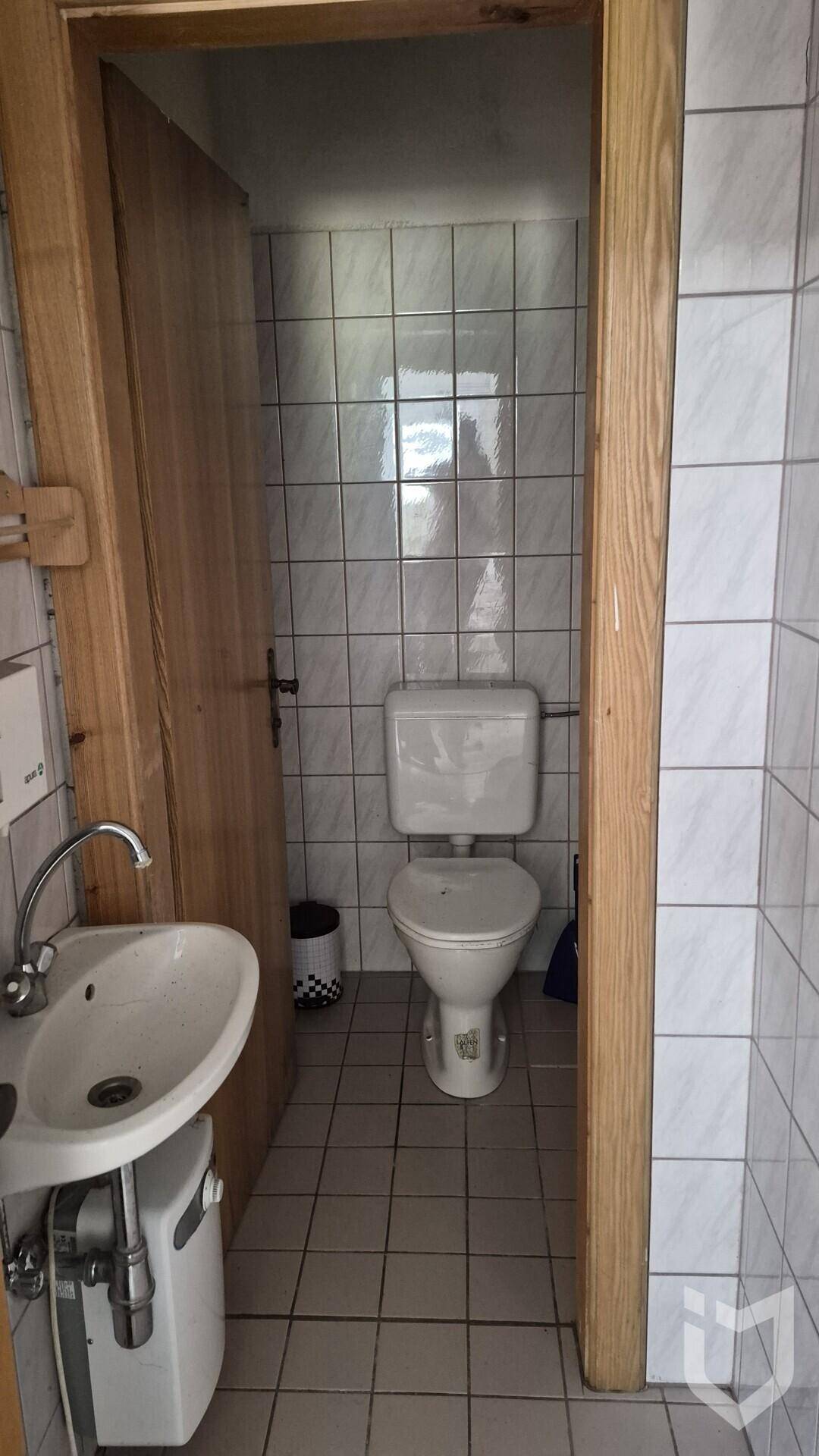 Kleiner Toilettenraum mit weißen Fliesen, WC und Waschbecken, ausgestattet mit einer Holztür.