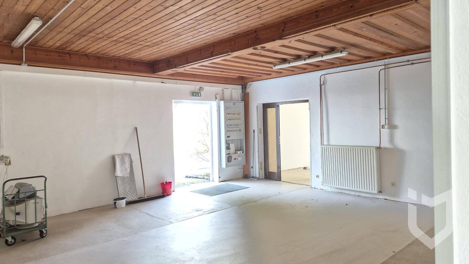 Leerer Raum mit Holzbalkendecke, weißen Wänden und Betonboden, bereit zur Nutzung.
