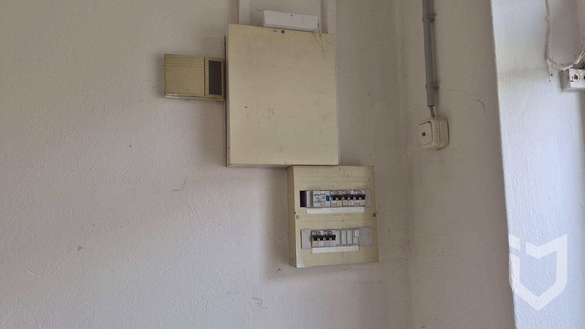 Kleinerer elektrischer Sicherungskasten an einer weißen Wand in einem Nebenraum.