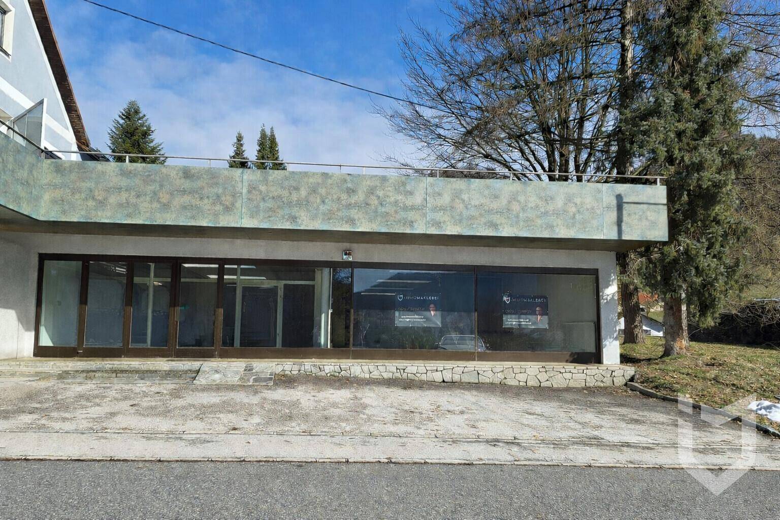 Moderne Gewerbefassade mit großen Glasfenstern und einem Flachdach in bergiger Umgebung.